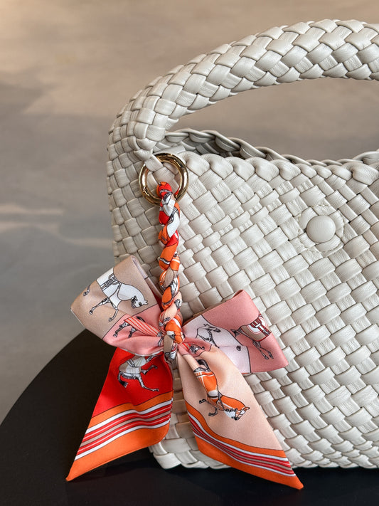 Braided Bow Charm in gedrehter Schleifenform, befestigt an einer Tasche – modischer Accessoire-Trend aus Twill in orangenem Muster