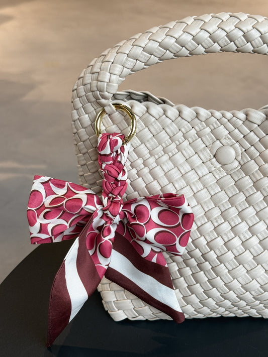 Braided Bow Charm in geflochtener Schleifenform, befestigt an einer Tasche – modischer Accessoire-Trend aus Twill in rotem Muster