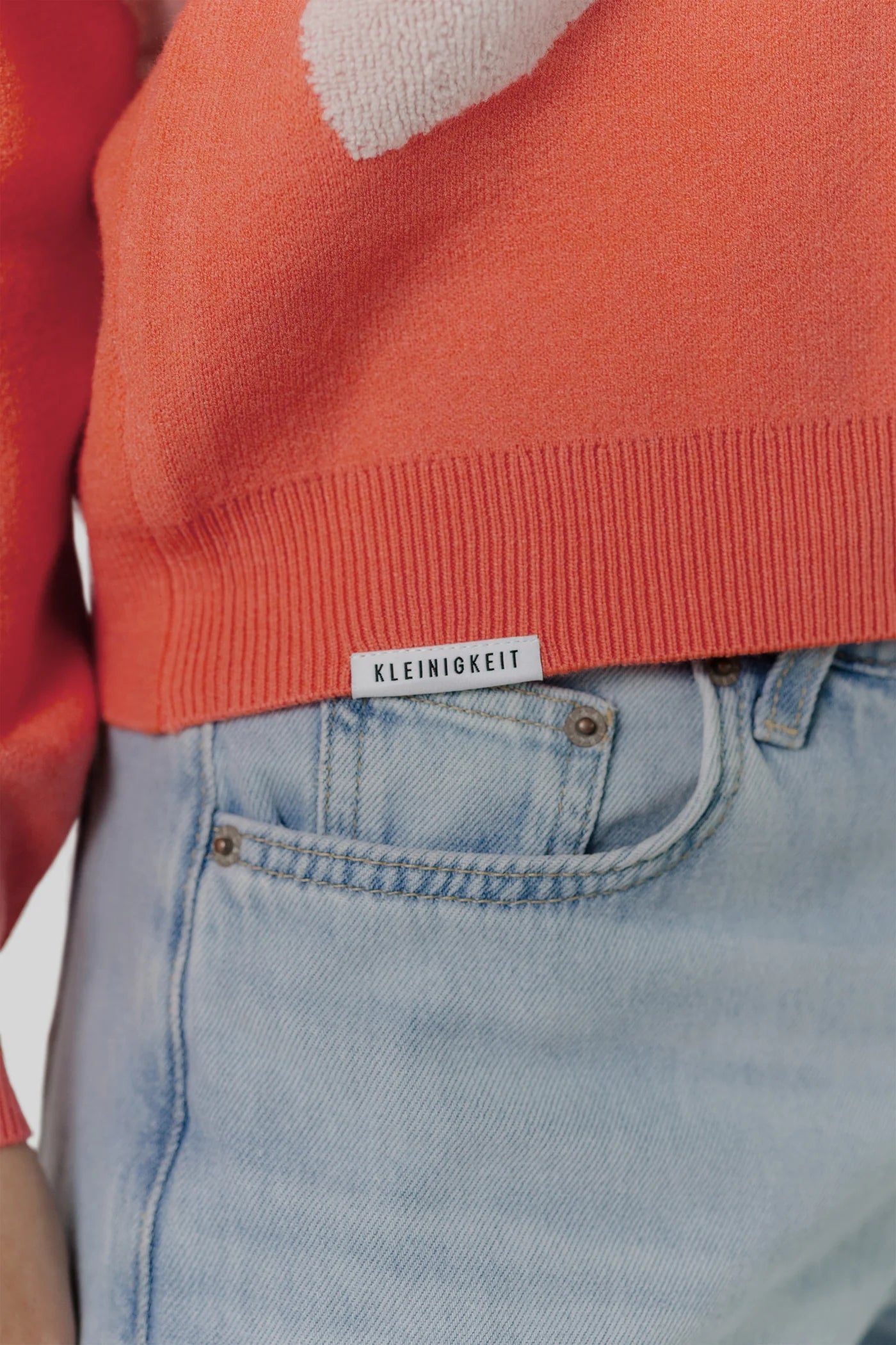 Nahaufnahme des Kleinigkeit Lovely Wollma Pullovers, zeigt das dezente Flaglabel an der Saumnaht und die hochwertige Verarbeitung.