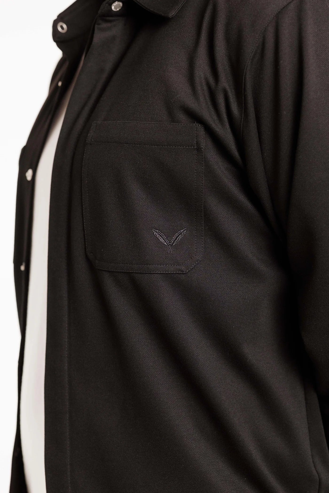 Detailansicht des Kleinigkeit Peter Maffein Shirts in klassischem Schwarz, zeigt die dezente Doppelfeder-Stickerei und die verdeckte Knopfleiste.