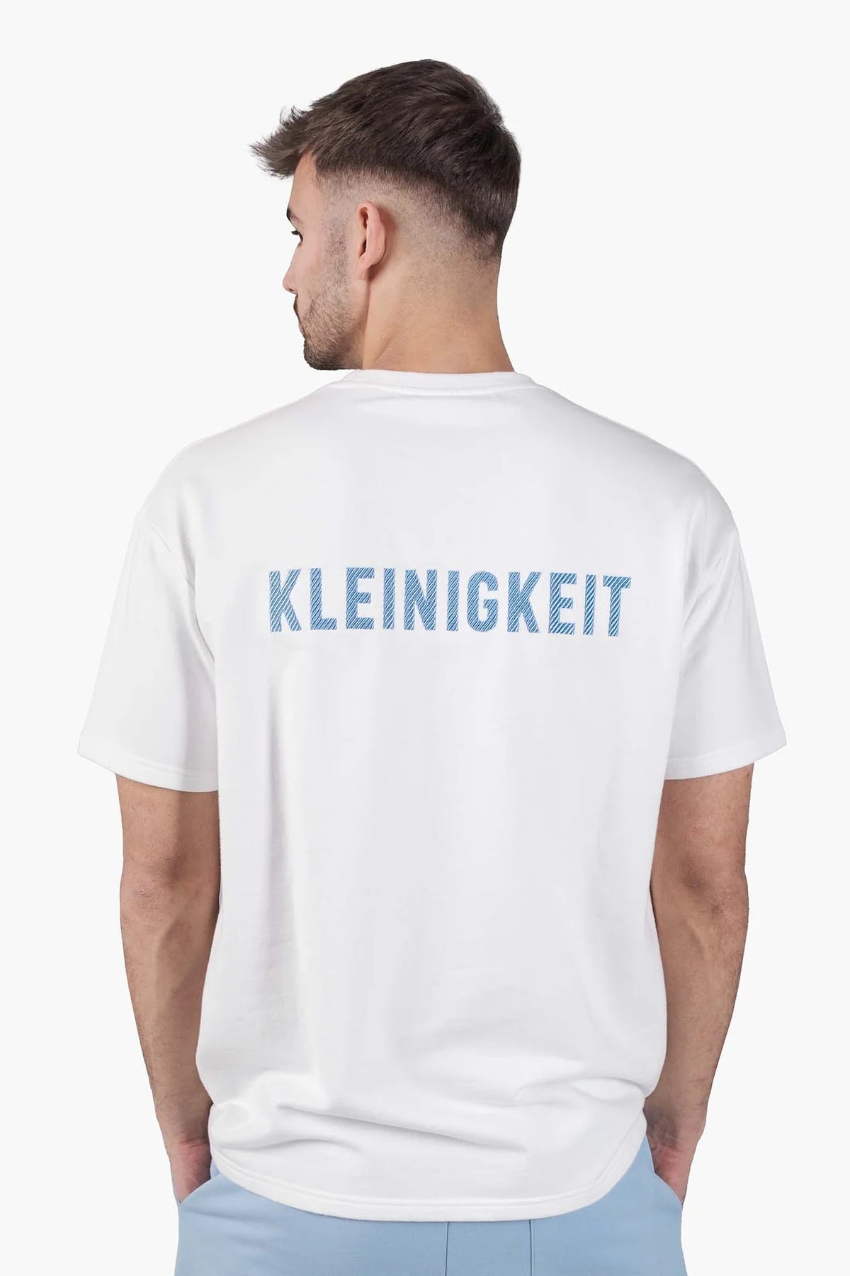 Rückansicht des Kleinigkeit Sticki Micki Shört White mit auffälligem KLEINIGKEIT Rückenstick, getragen von einem Model