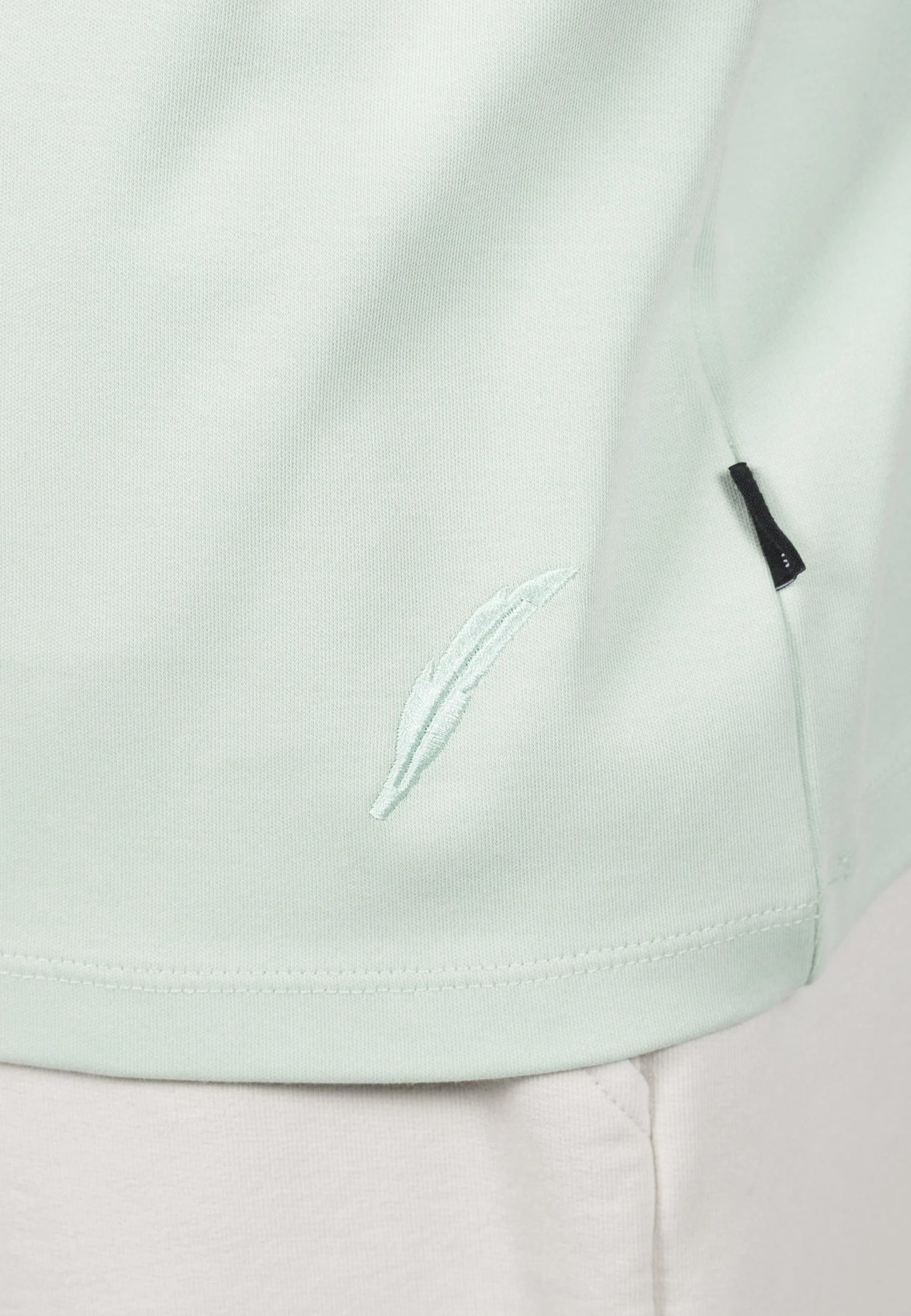 Kleinigkeit Unterragendes Shört - Matcha Green Detailaufnahme mit dezenter Stickerei am Saum und kleinem Label-Tag an der Seite