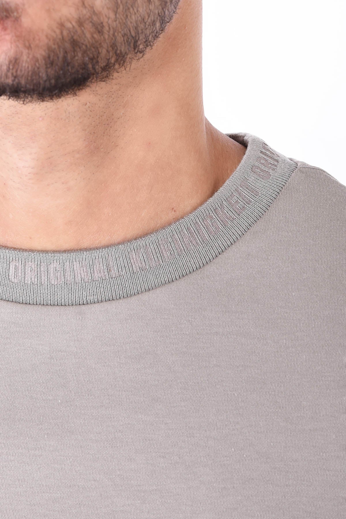 Nahaufnahme des gerippten Kragens vom Kleinigkeit Unterragendes Shört in Olive mit eingeprägtem Schriftzug. Stilvolle Details für einen hochwertigen Look.