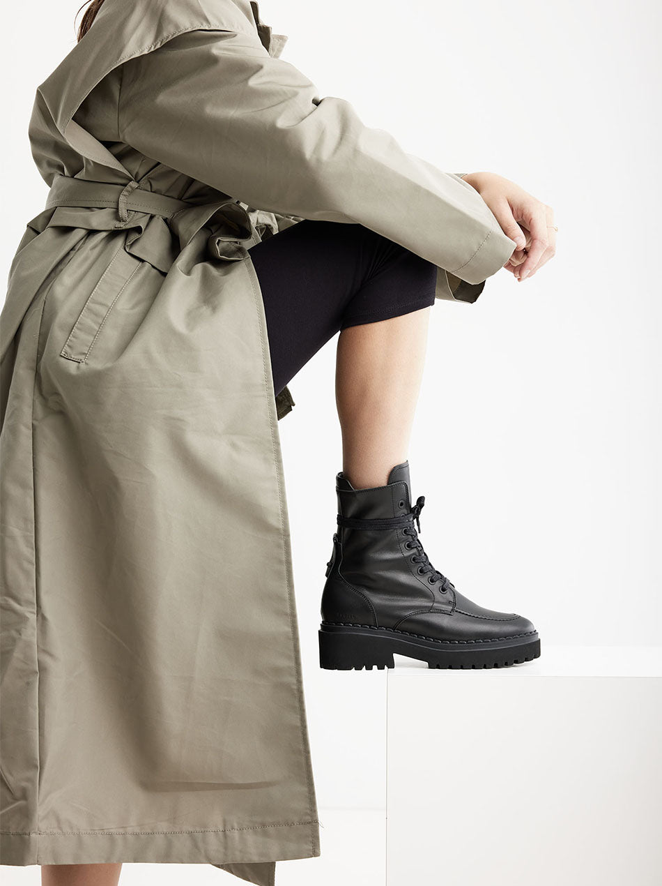 Stylischer Nubbik Fae Bobbi Stiefel kombiniert mit einem langen Trenchcoat, perfekt für ein urbanes Outfit.