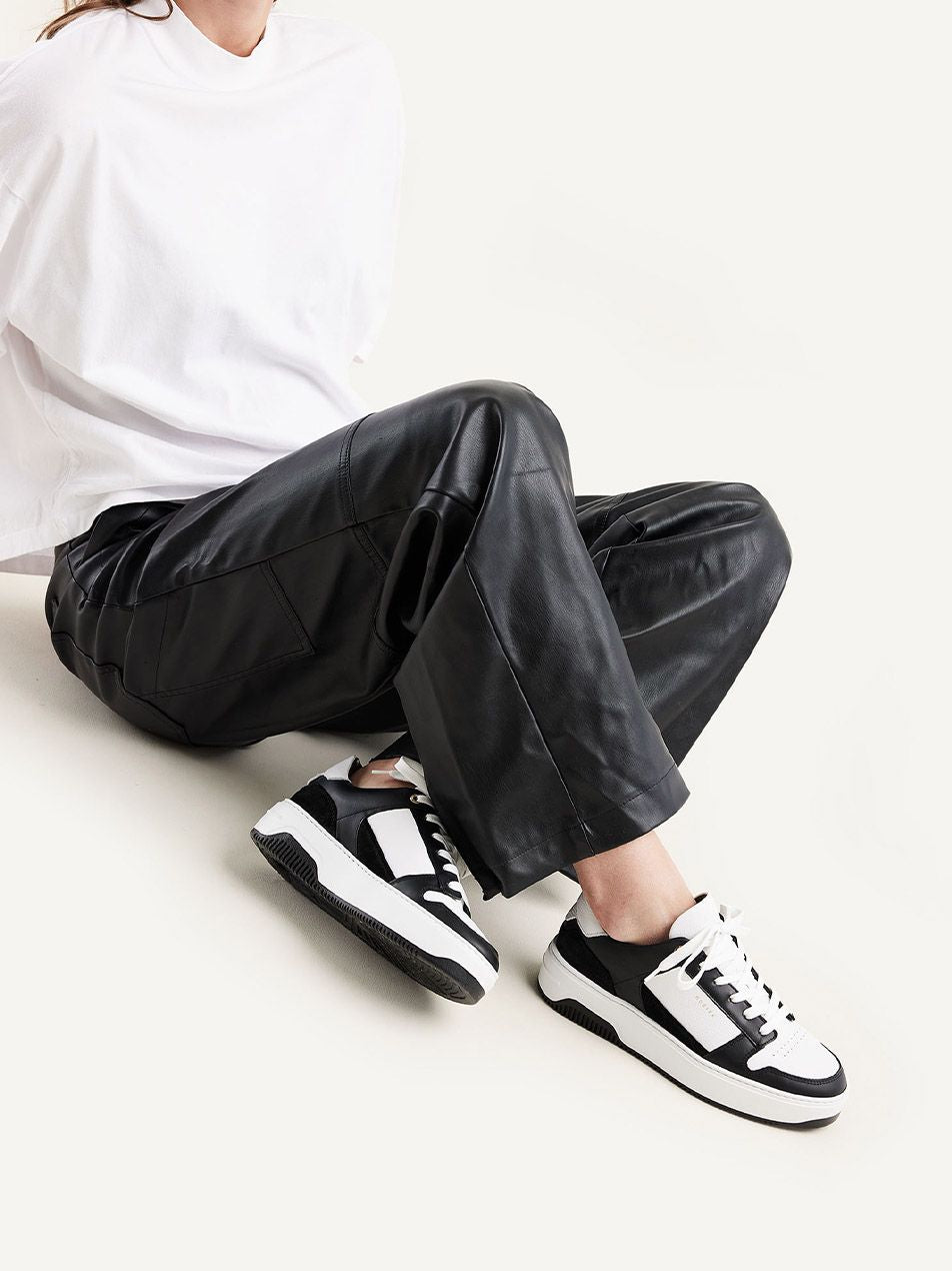 Frau trägt die Nubbik Basket Court Sneaker in Schwarz und Weiß, kombiniert mit lässigem Look aus Lederhose und weißem Shirt.