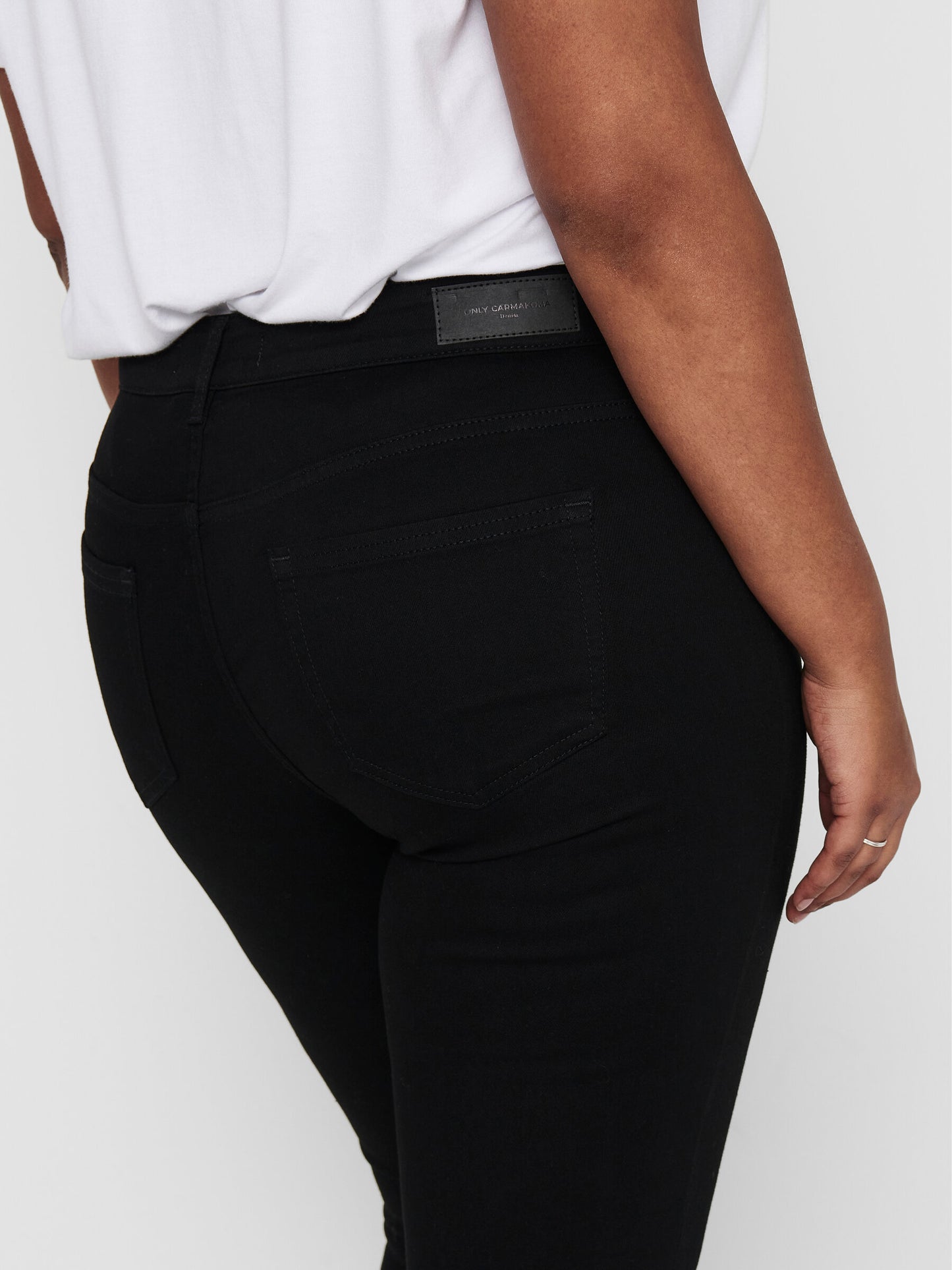 Nahaufnahme der Rückseite der Only Carmakoma Carwilly Skinny Black Jeans, getragen von einem Model. Fokus auf Gesäßtaschen und das schwarze Logo-Patch am Bund.