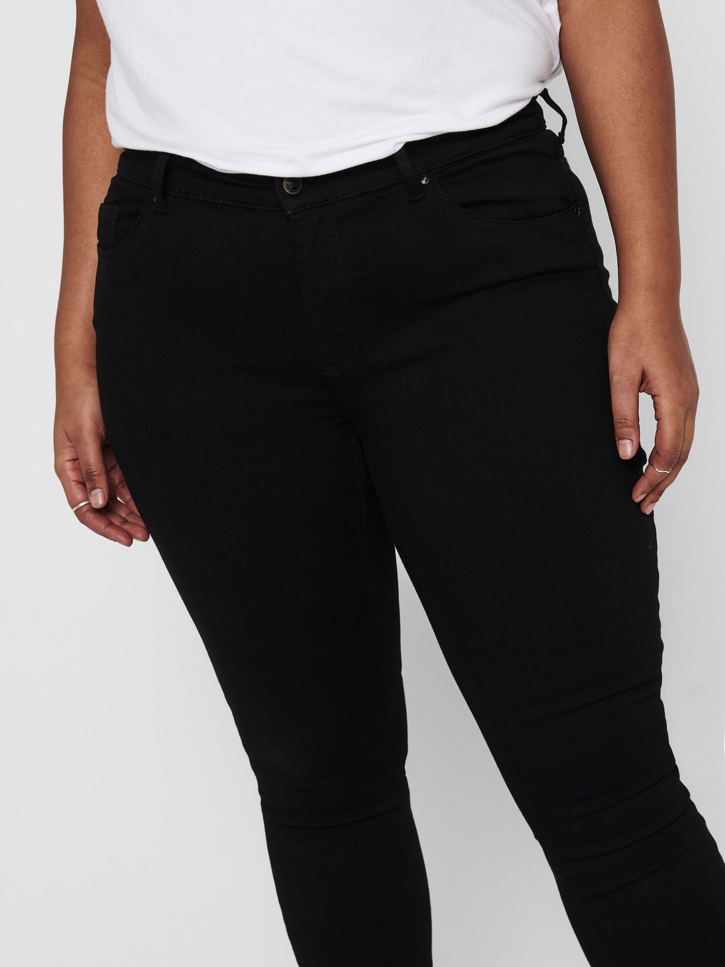 Nahaufnahme der Vorderseite der Only Carmakoma Carwilly Skinny Black Jeans, getragen von einem Model. Der mittelhohe Bund und die schlichte schwarze Optik betonen die Figur.
