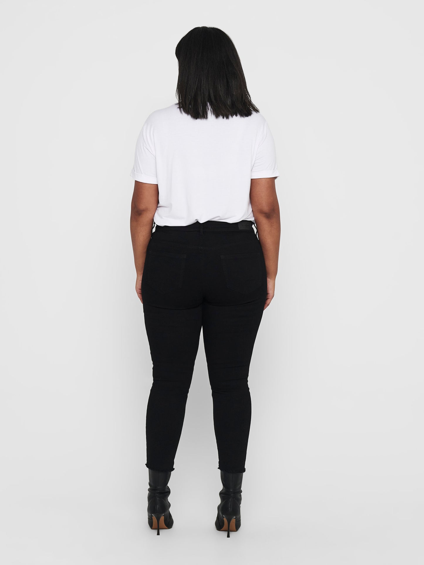 Rückansicht der Only Carmakoma Carwilly Skinny Black Jeans, getragen von einem Model mit weißem Shirt und schwarzen Boots. Perfekte Passform von der Taille bis zu den Knöcheln.
