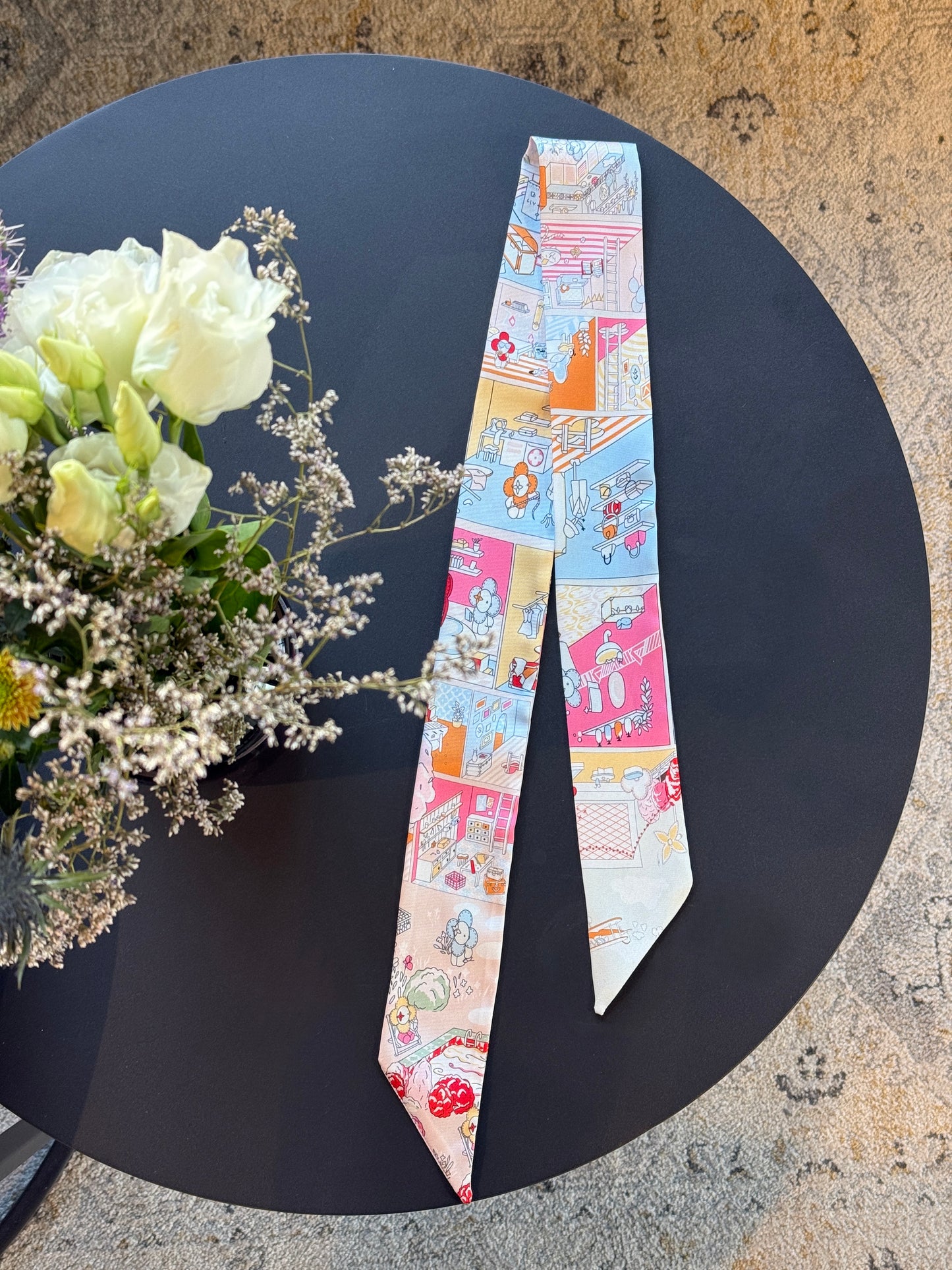 Hochwertiges Twilly Urban Sunset aus Seide mit detailreichem Stadtmotiv in warmen Orange-, Gelb- und Rosatönen, perfekt als Accessoire für Taschen oder Haare.