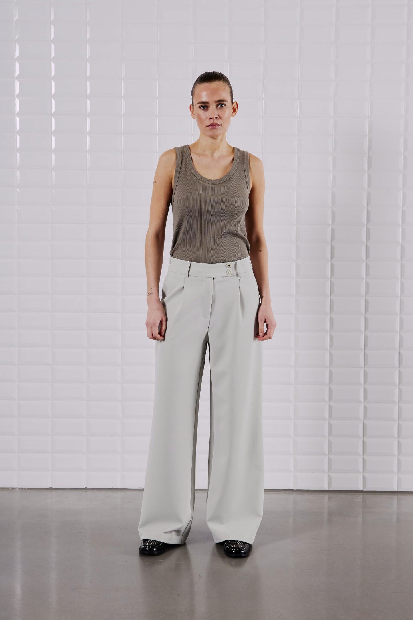 Model trägt das WithBlack Lulu Tank Top Light Stone Grey kombiniert mit einer weiten Stoffhose in Beige.