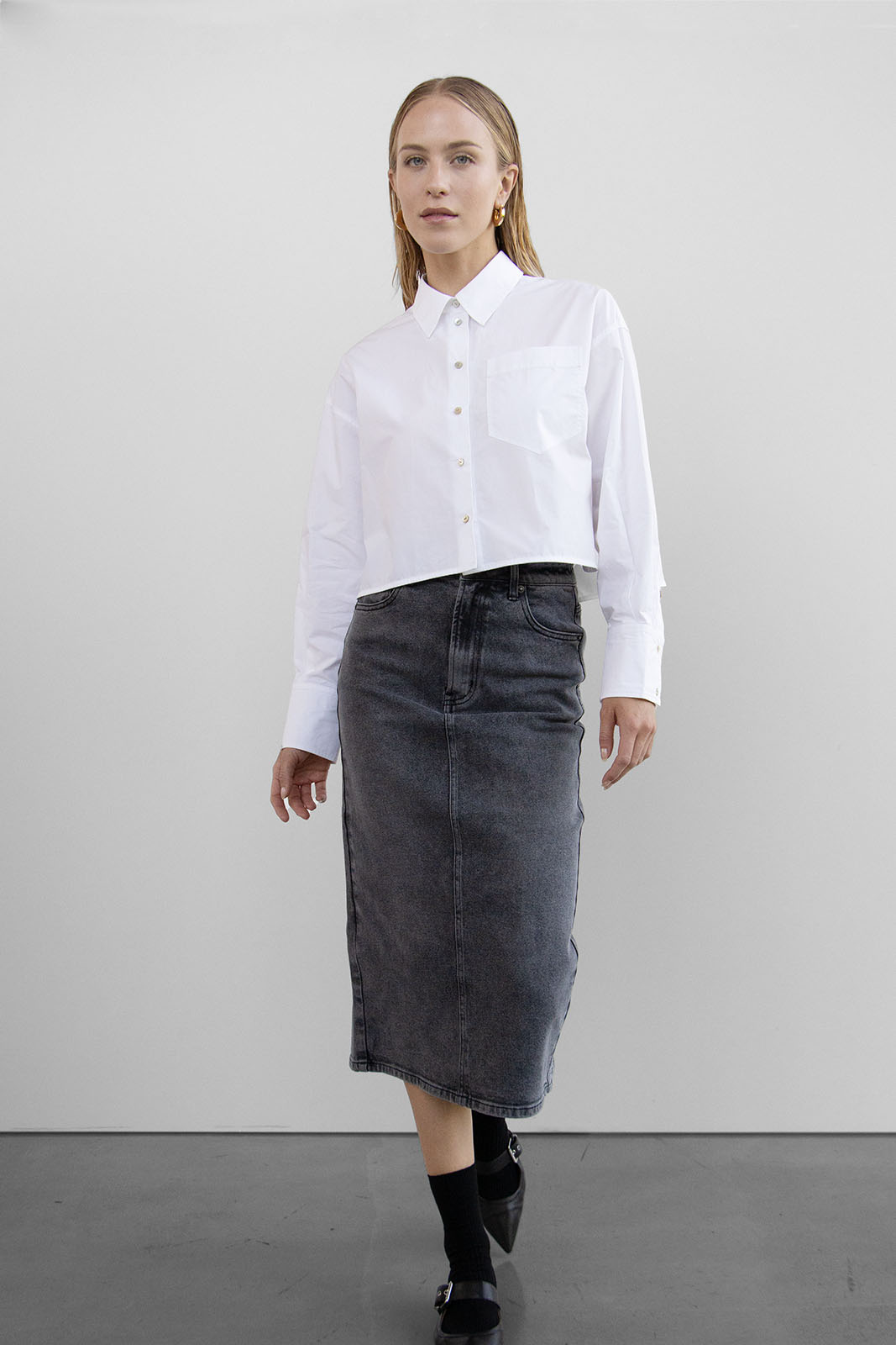 Frontansicht des WithBlack Shortly Cropped Shirts in Weiß, mit kastenförmigem Schnitt und Brusttasche, kombiniert mit einer schwarzen Jeansrock.