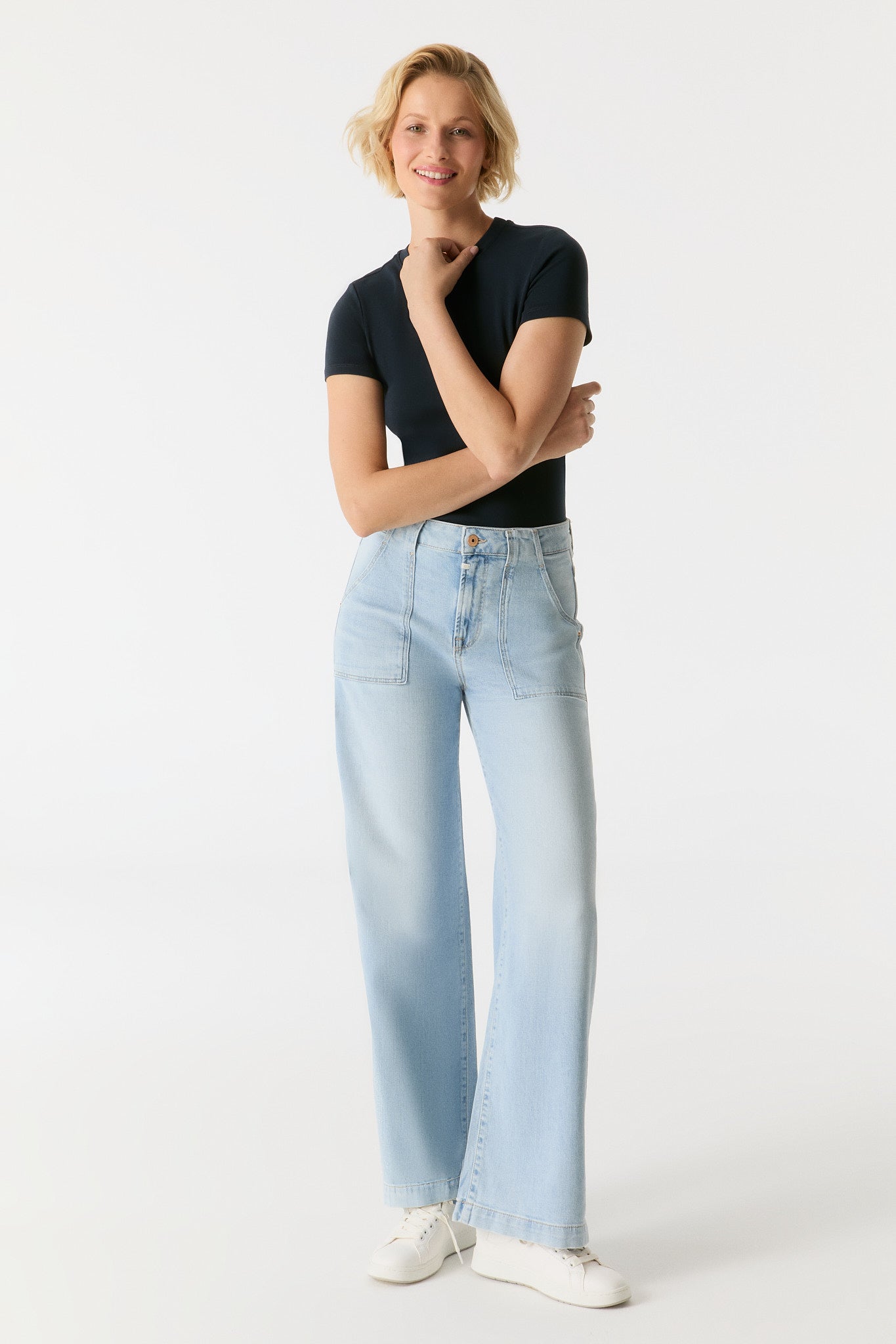 Model trägt die COJ Lulu Wide Leg Aqua Blue Jeans in voller Länge, kombiniert mit einem schwarzen Shirt und weißen Sneakern.