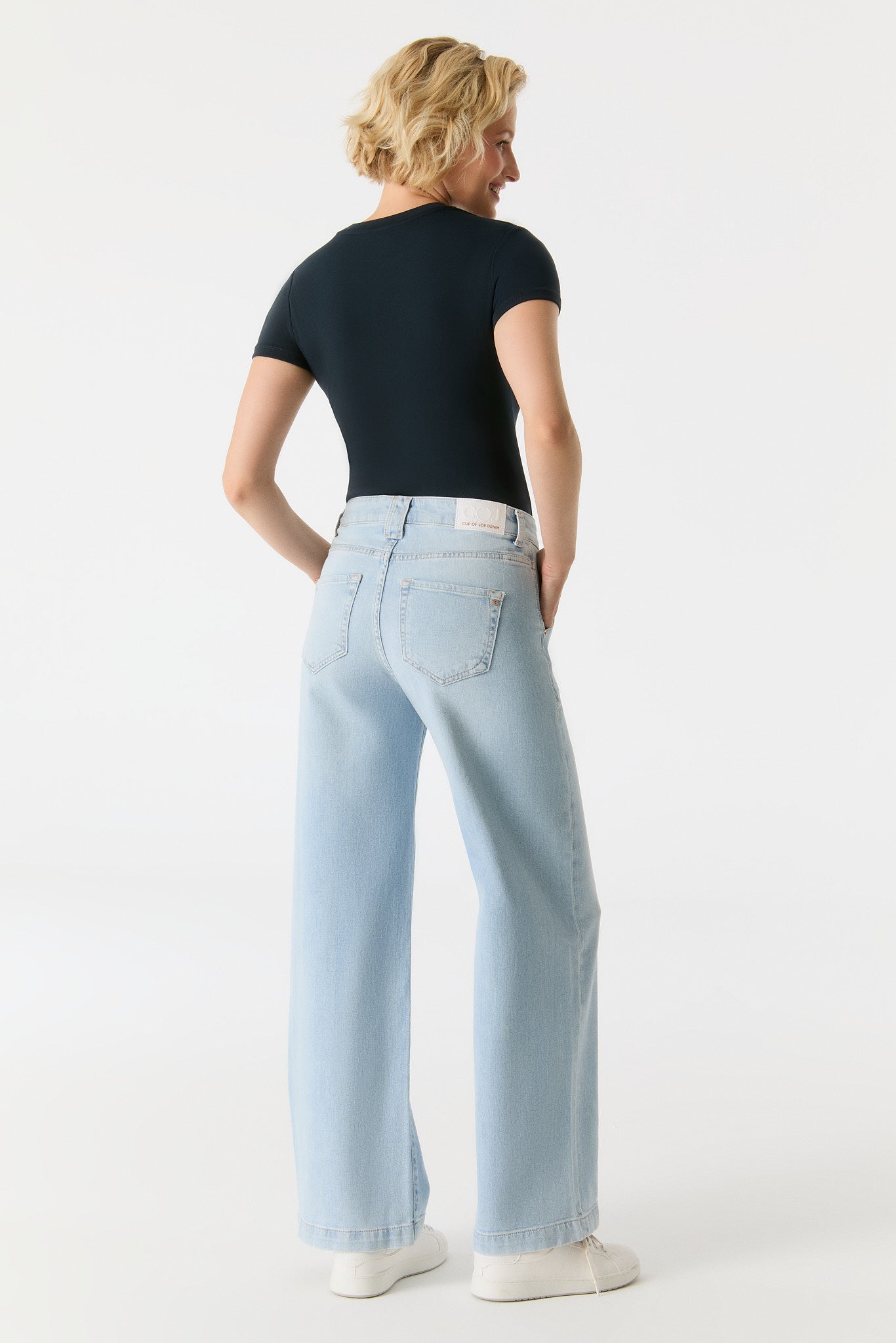 Rückansicht der COJ Lulu Wide Leg Aqua Blue Jeans, getragen mit einem schwarzen Shirt und weißen Sneakern.