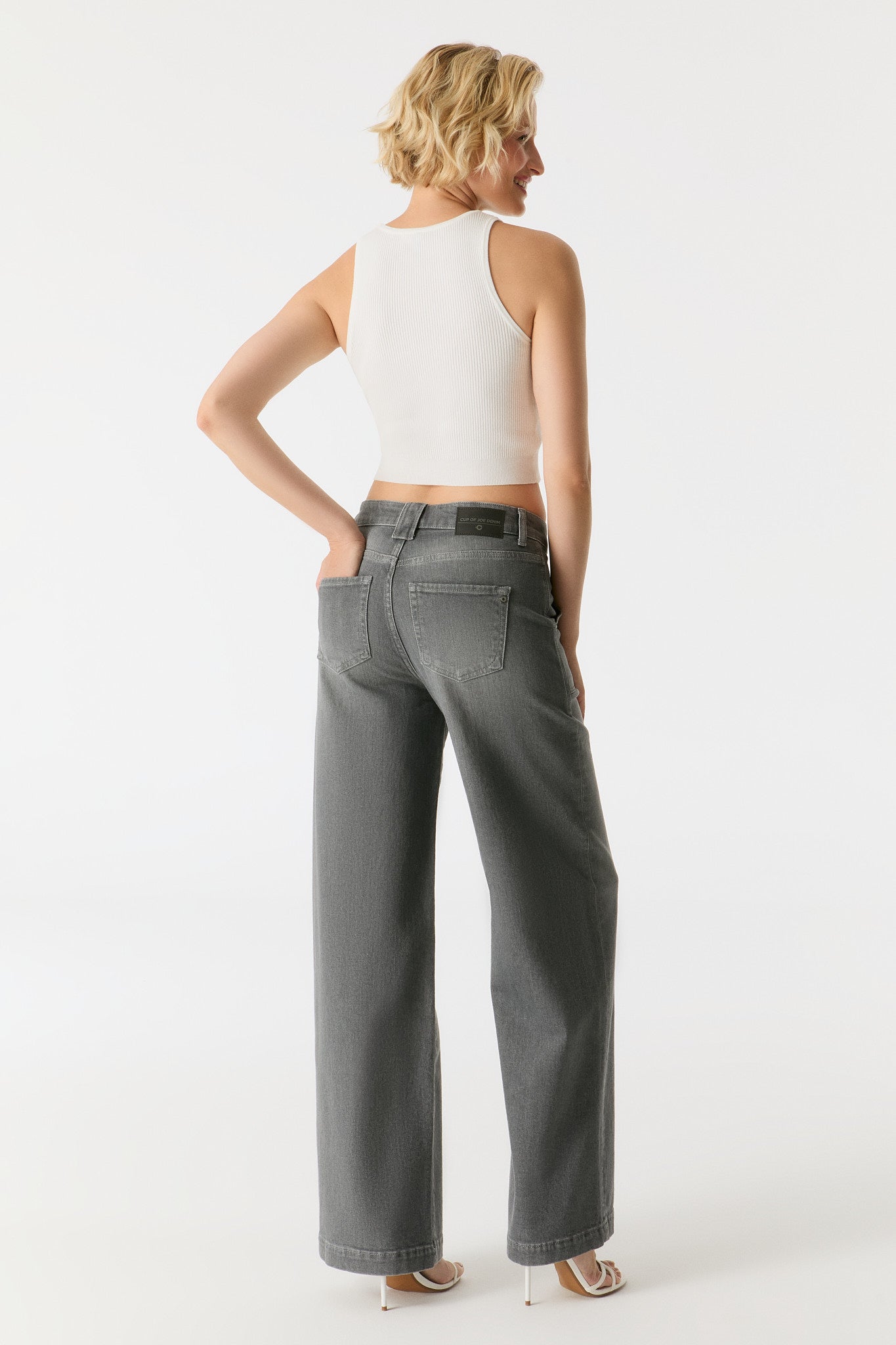Rückansicht der COJ Lulu Wide Leg Jeans in Grey Vintage, getragen von einem Model, kombiniert mit einem weißen Crop-Top.