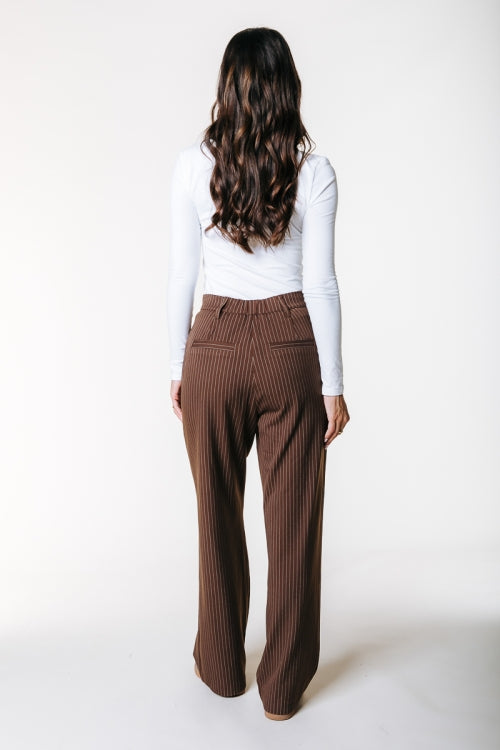 Rückansicht der Colourful Rebel Rus Pinstripe Straight Pants - Brown, getragen von einem Model mit weißem Langarmshirt.