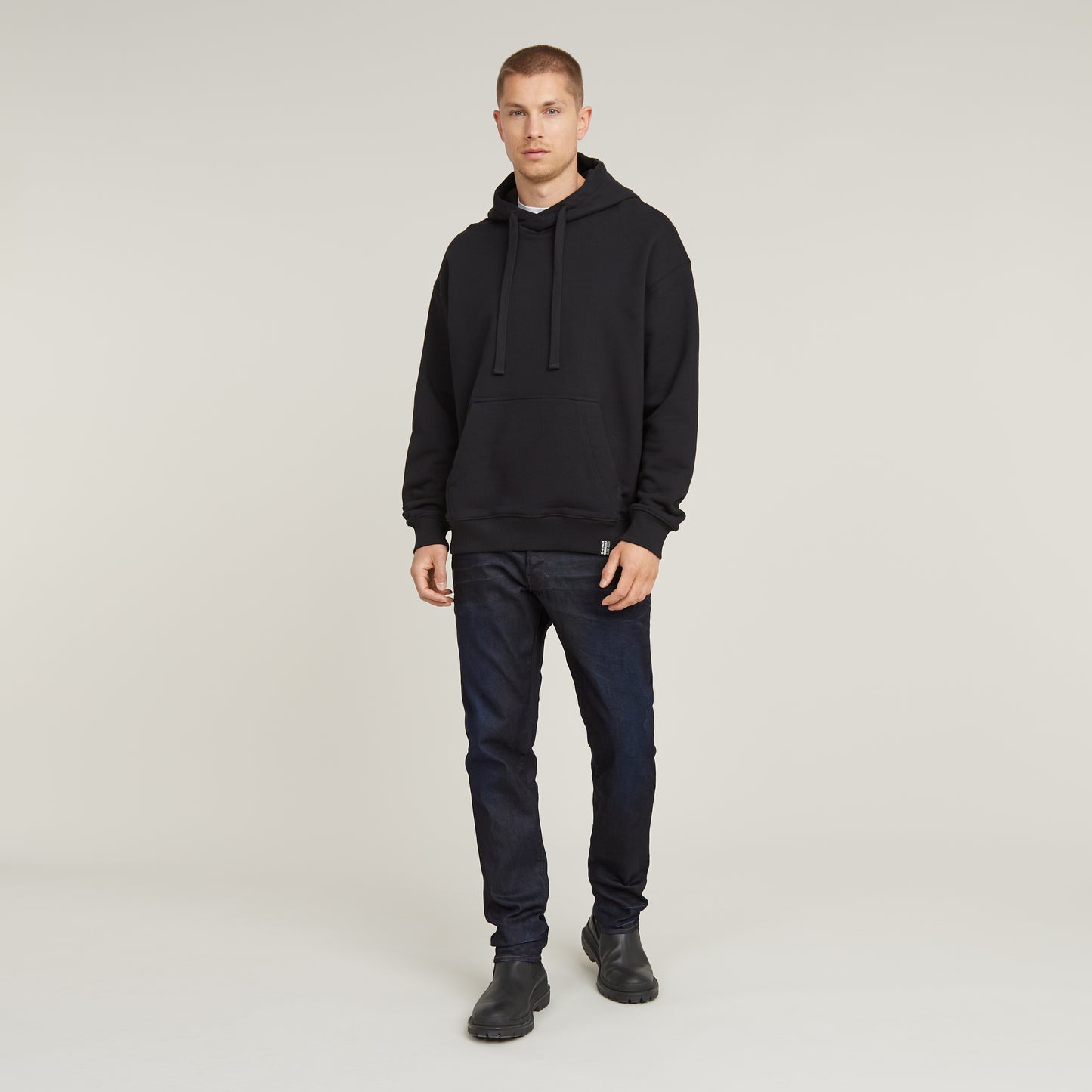 Modell trägt G-Star 3301 Regular Tapered Dark Aged Jeans mit schwarzem Hoodie und Boots.