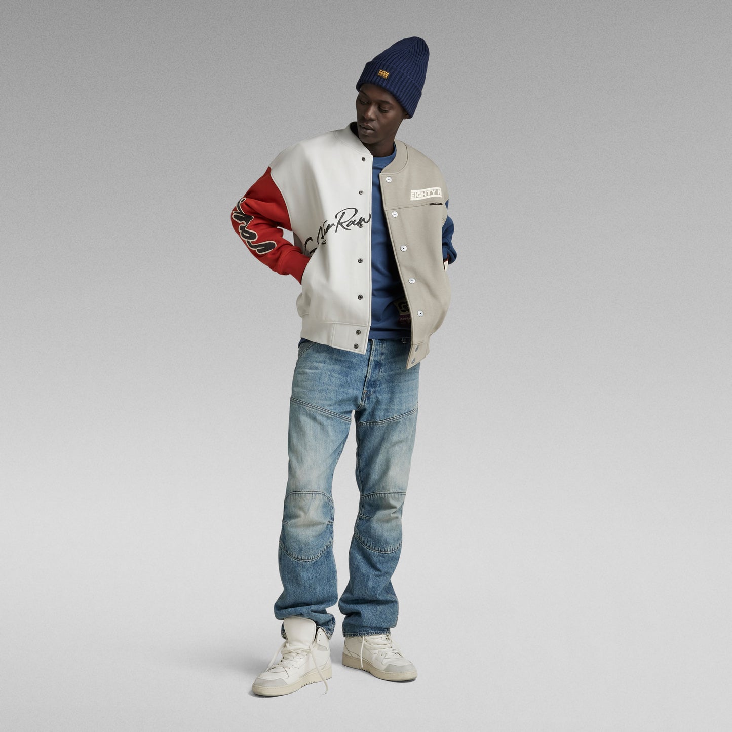 Modell trägt G-Star Elwood Regular Antique 96 Jeans mit Colorblock-Jacke und Beanie.