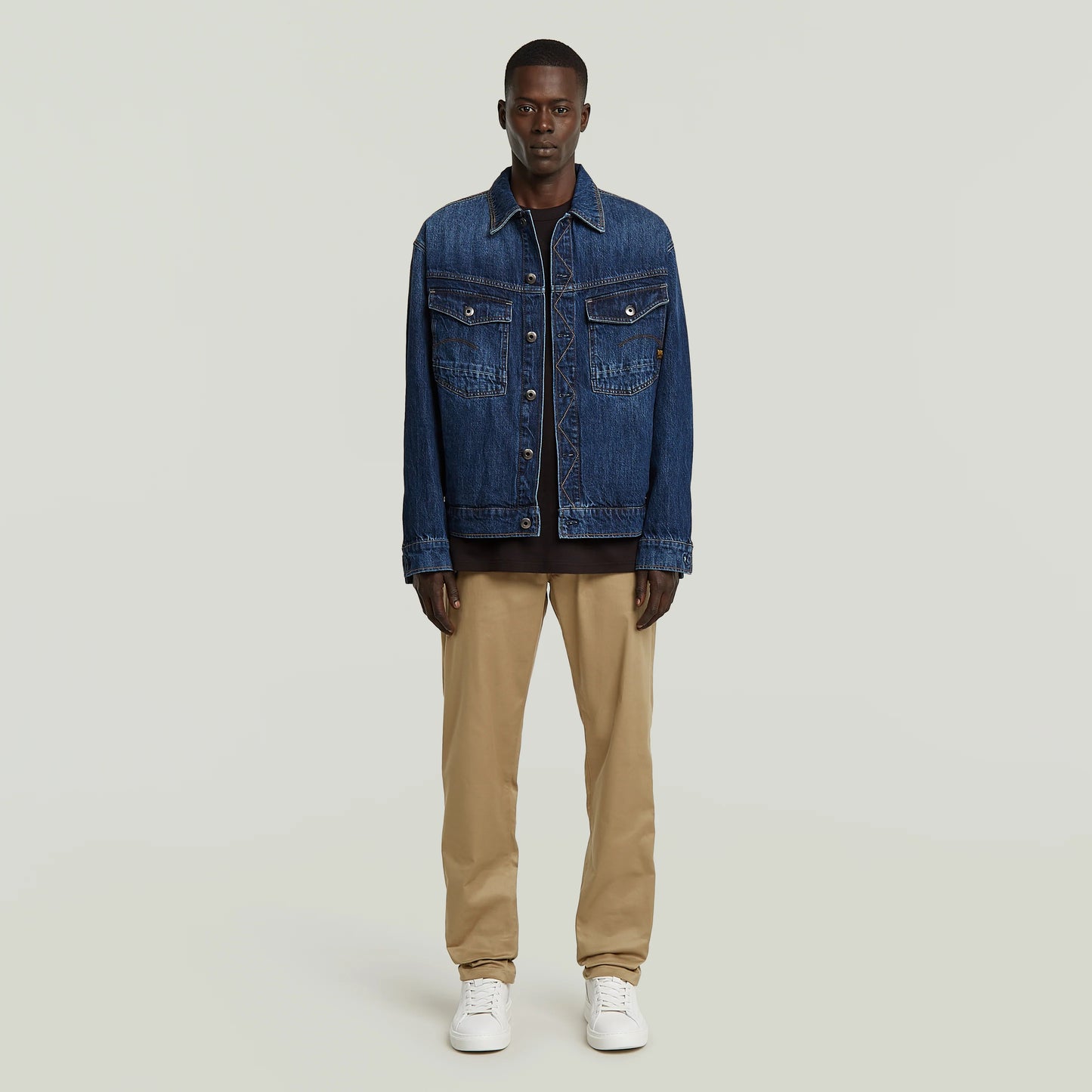 Modell trägt G-Star Morry Tapered Chino Safari mit dunkler Denimjacke und weißen Sneakers.