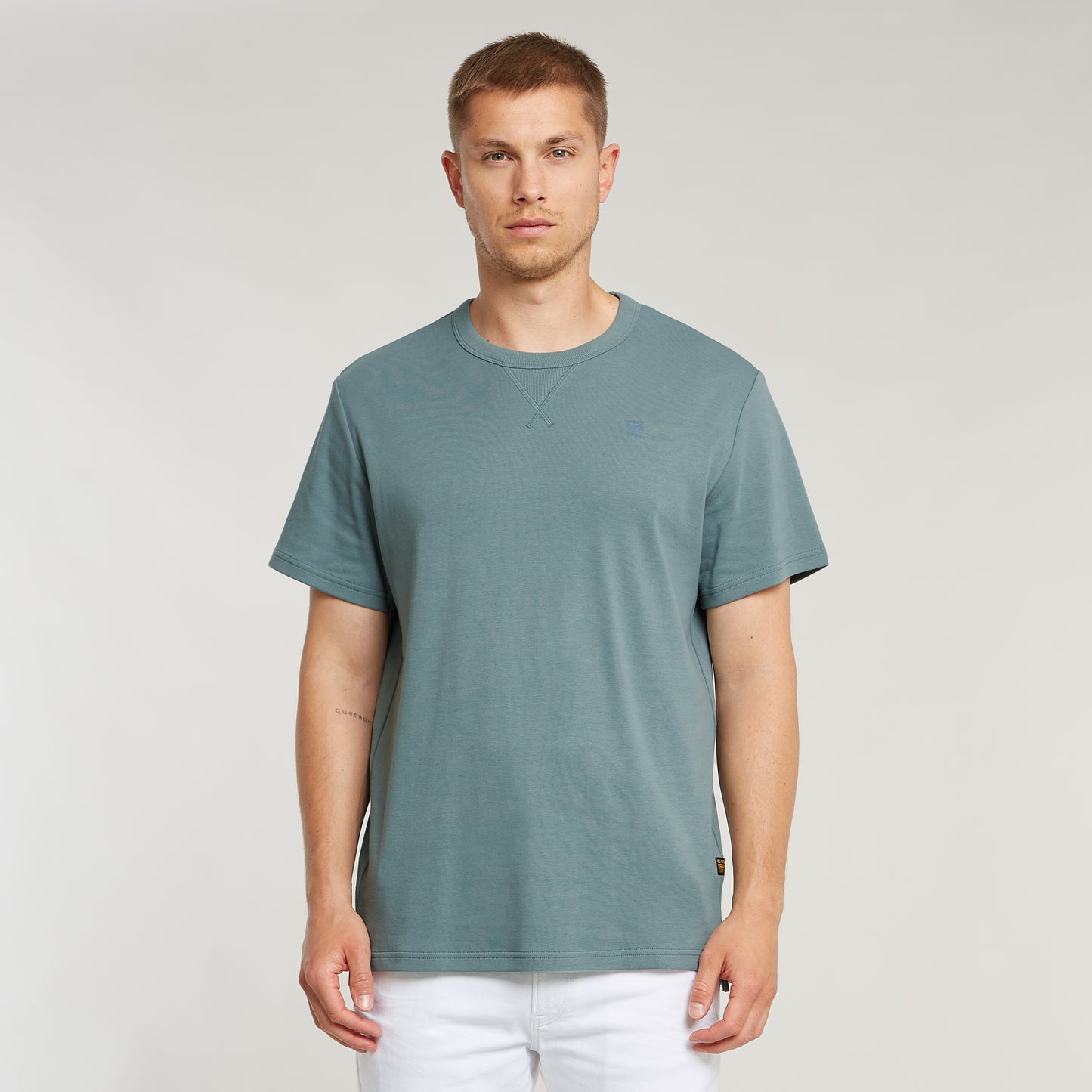 Model trägt das G-Star Nifous T-Shirt in Bolt Grey mit weißer Hose, zeigt die Passform und den Schnitt des Shirts.
