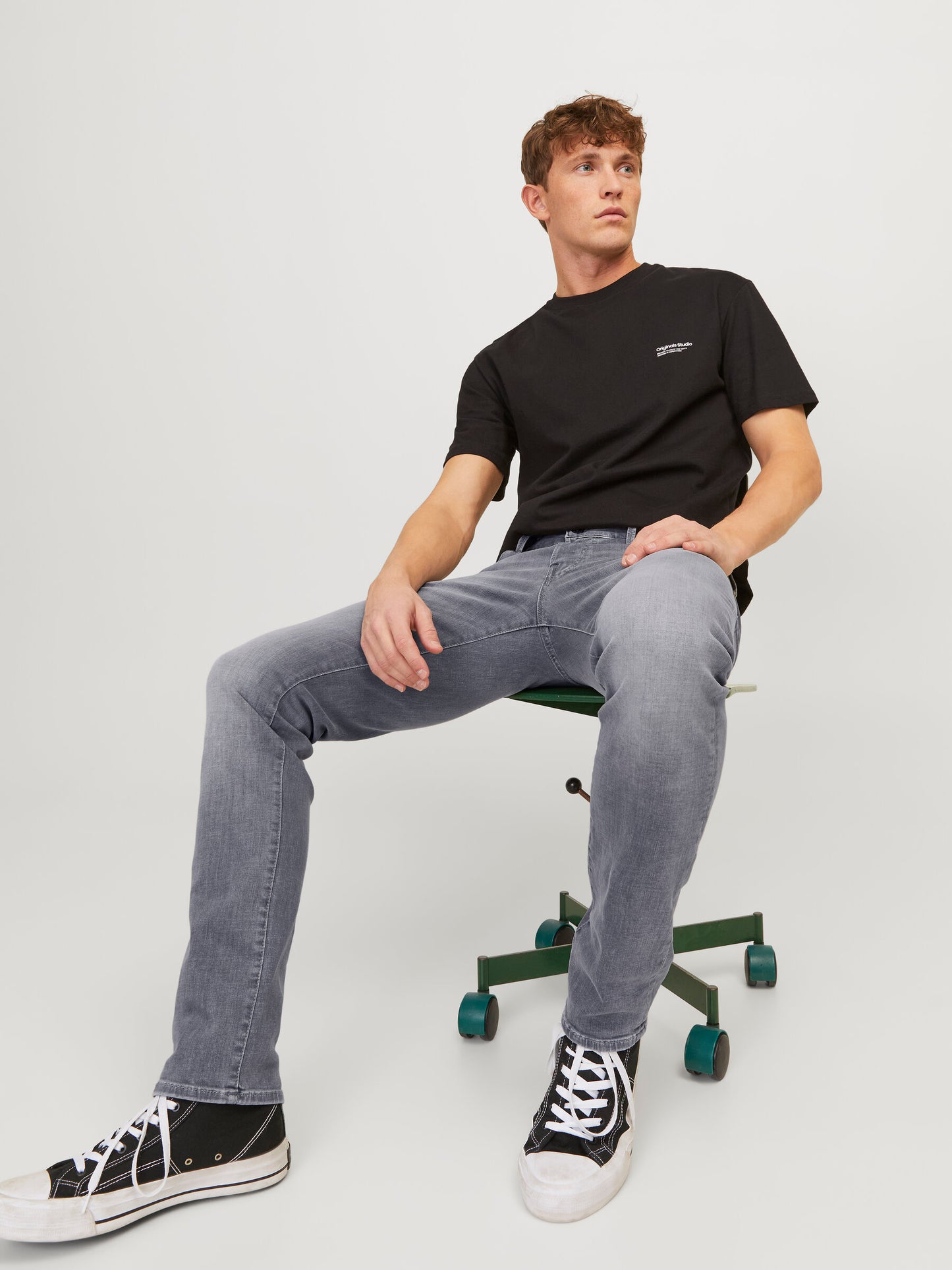 Model, das die Jack & Jones Glenn Slim Grey Denim trägt und lässig auf einem Bürostuhl sitzt.