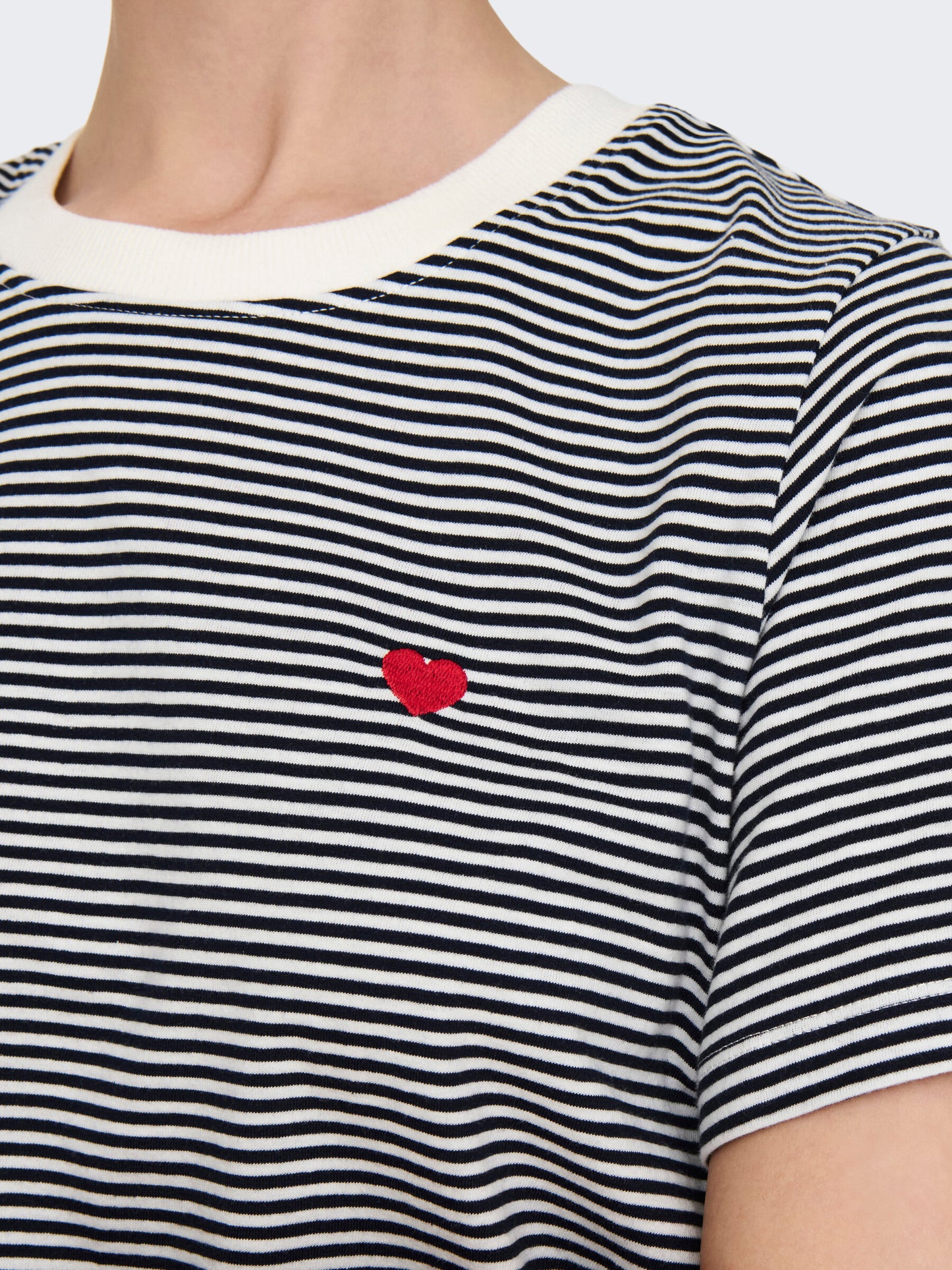 Nahaufnahme des JDY Pisa Tops in der Farbe Cloud Dancer Sky Captain Stripes mit rotem Herz-Detail auf der Brust. Die feinen Streifen und das kleine gestickte Herz setzen dezente Akzente.