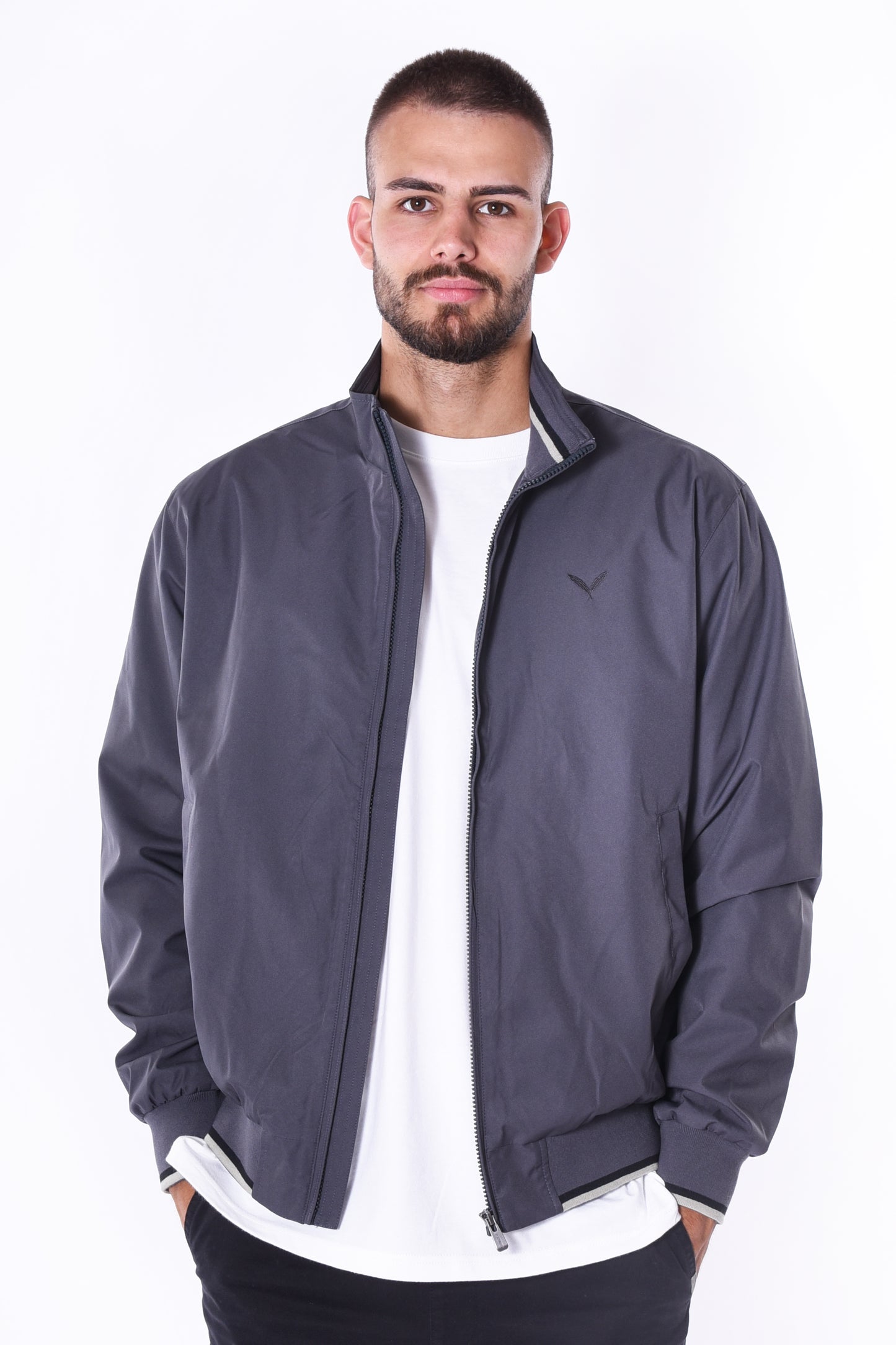 Modell trägt die Kleinigkeit Signature Jacket Ashphalt Grey mit Stehkragen, gerippten Abschlüssen und dezentem Ton-in-Ton Feather-Logo auf der Brust.