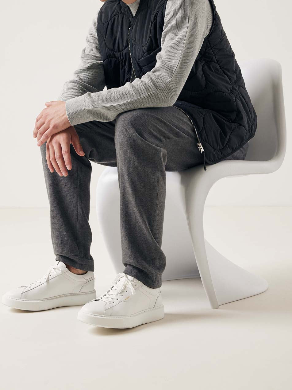 Nubbik Vince Tora White – gestylte Aufnahme mit Sneakern, kombiniert zu einem lässigen Look mit grauer Hose und schwarzer Weste.
