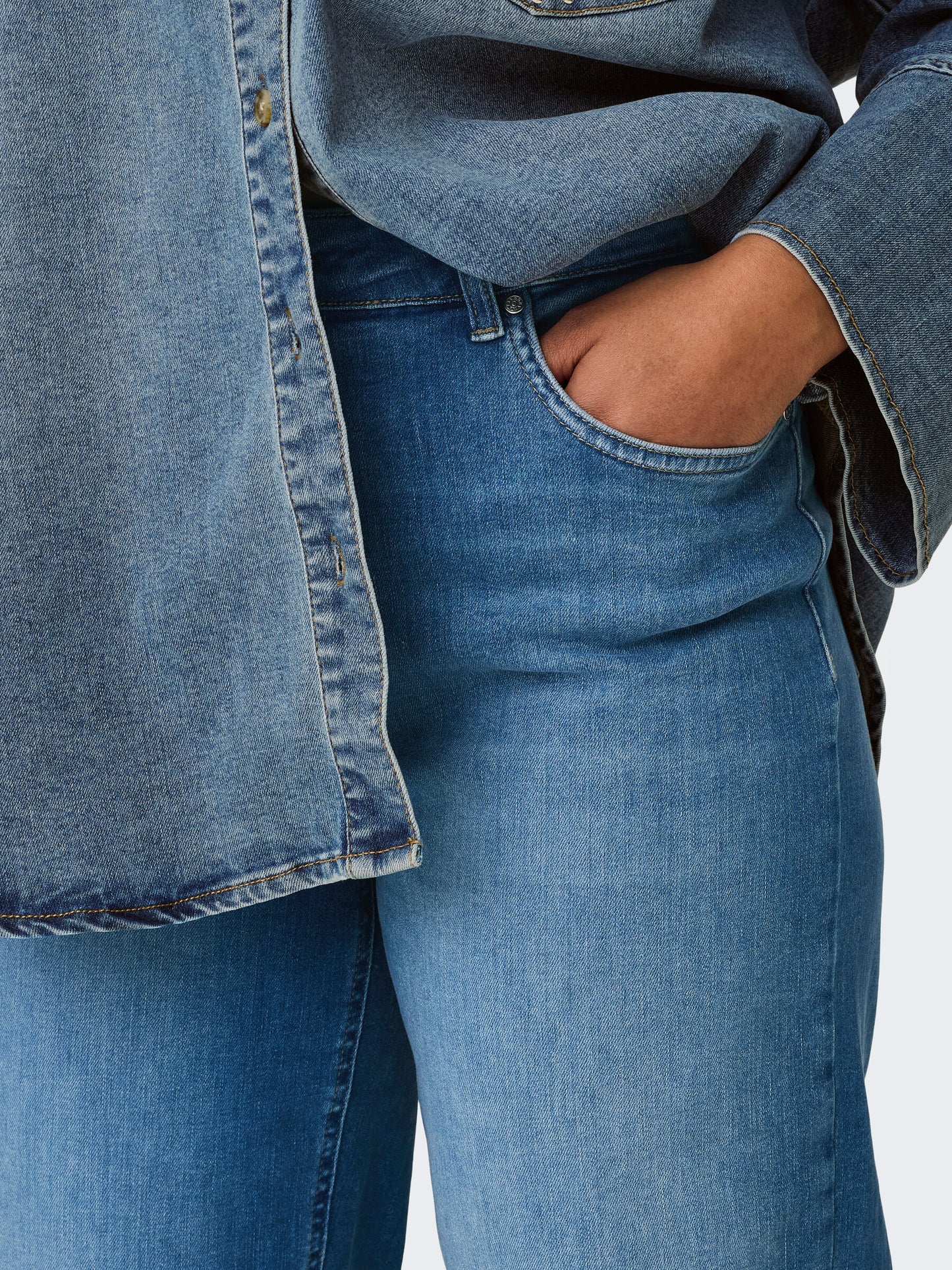 Nahaufnahme der vorderen Tasche und Gürtelschlaufen der Only Carmakoma Carwilly wide fit Jeans in Medium blau. Perfekt für einen stilvollen Alltagslook.