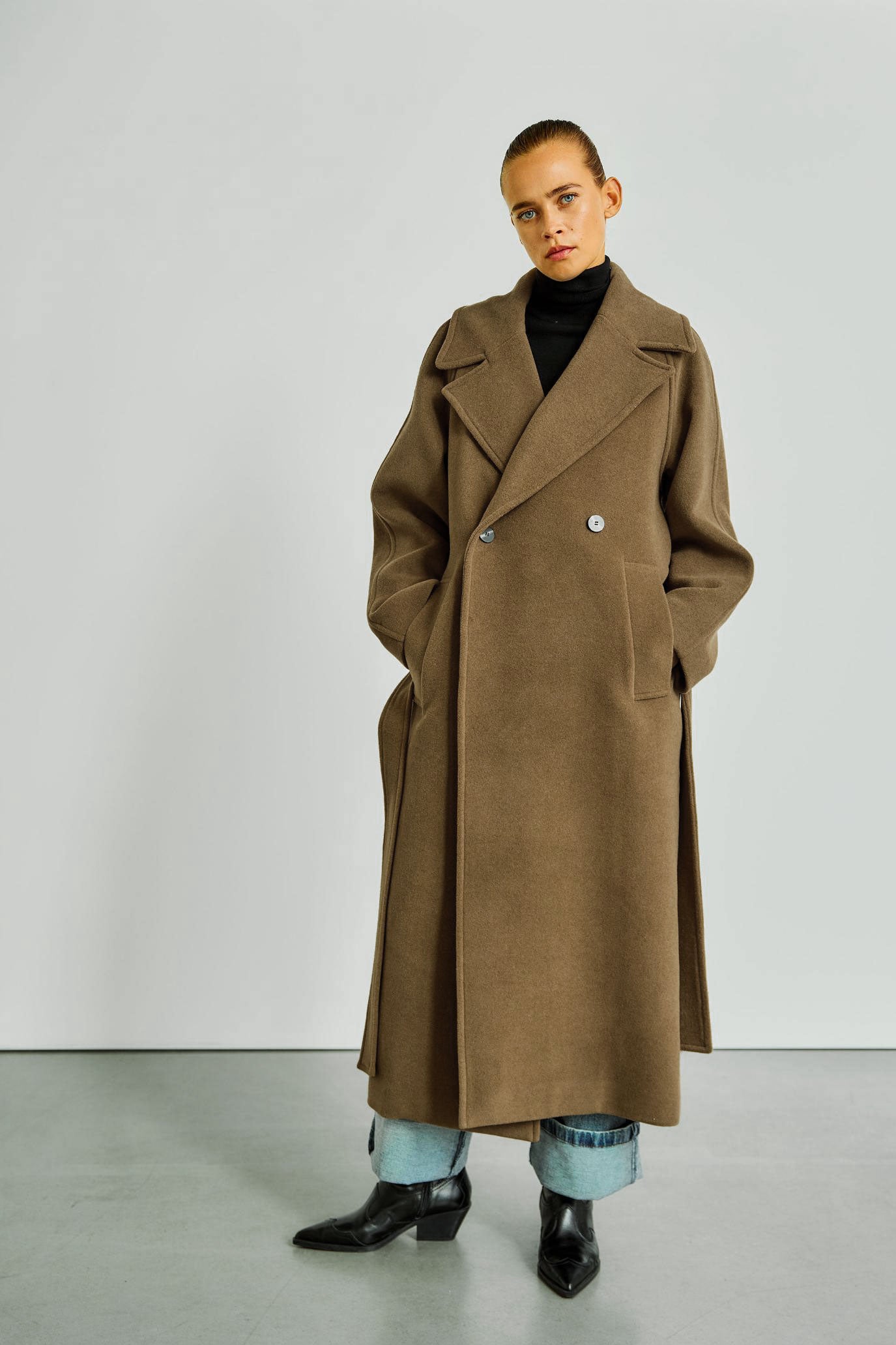 Frau präsentiert den WithBlack Brooklyn Wollmantel in Monks Robe mit zweireihiger Knopfleiste und eleganter Passform.