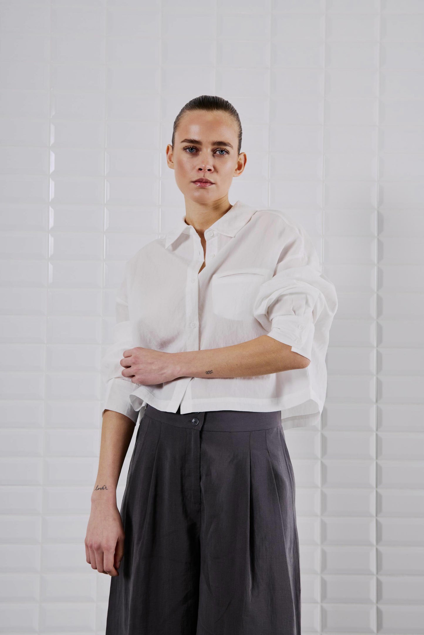 Frontansicht des WithBlack Quinie Cropped Shirt White, locker geschnitten mit Brusttasche, kombiniert mit weiter schwarzer Hose.