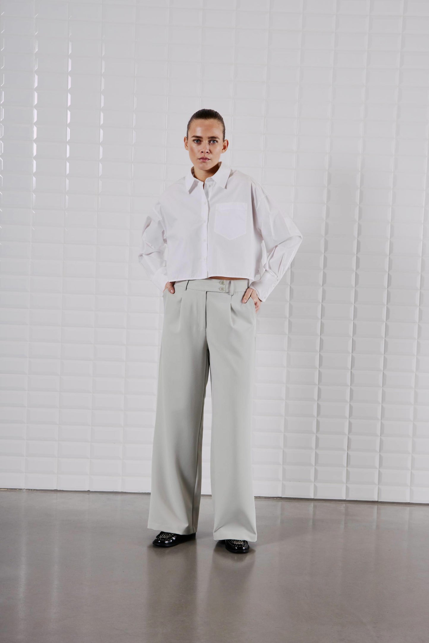 Model trägt das WithBlack Shorty Soft Cropped Shirt in Weiß, kombiniert mit einer weiten Stoffhose.