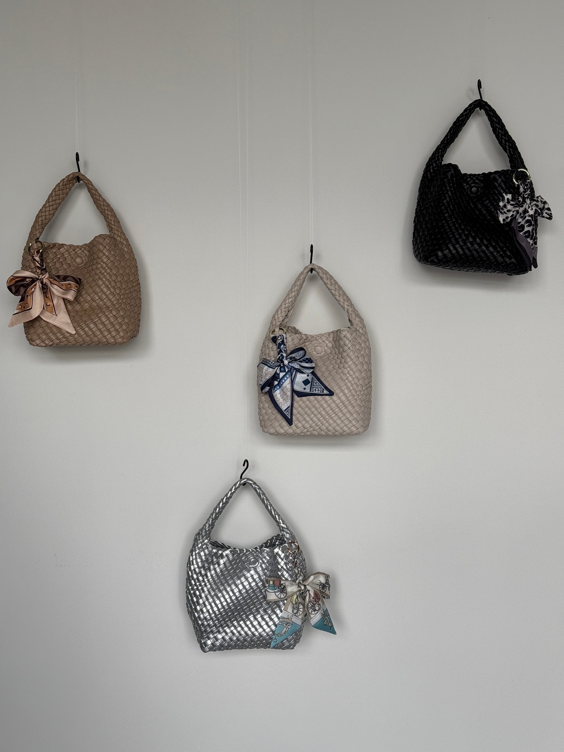 Vier Braided Mini Bags in verschiedenen Farben – Beige, Silber, Creme und Schwarz – mit dekorativen Halstüchern, stilvoll an der Wand präsentiert.