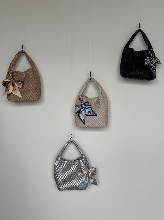 Vier Braided Mini Bags in verschiedenen Farben – Beige, Silber, Creme und Schwarz – mit dekorativen Halstüchern, stilvoll an der Wand präsentiert.