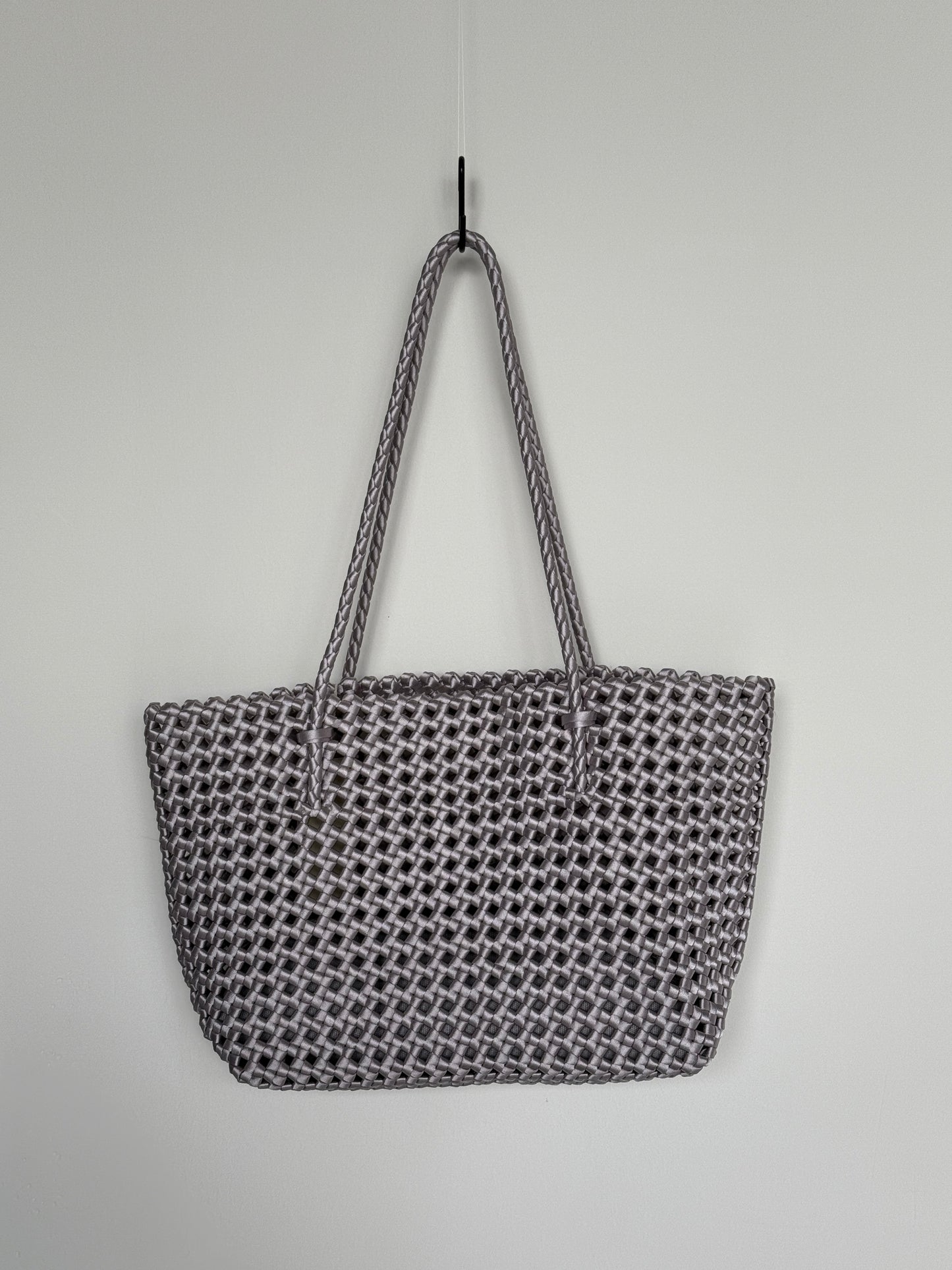 Geflochtene Braided Shopper Bag in Metallic-Silber mit langen Henkeln aus Stoff, an Haken aufgehängt