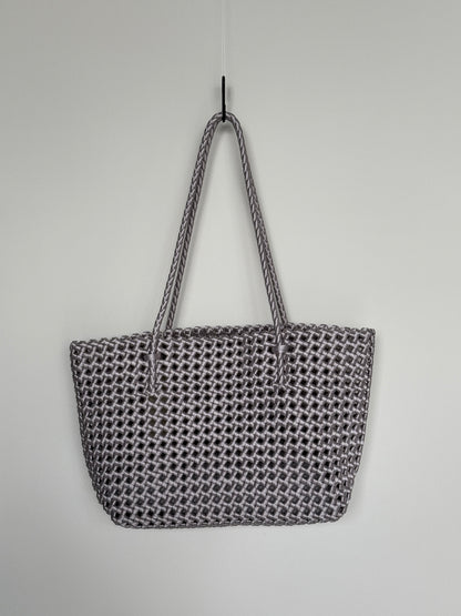 Geflochtene Braided Shopper Bag in Metallic-Silber mit langen Henkeln aus Stoff, an Haken aufgehängt