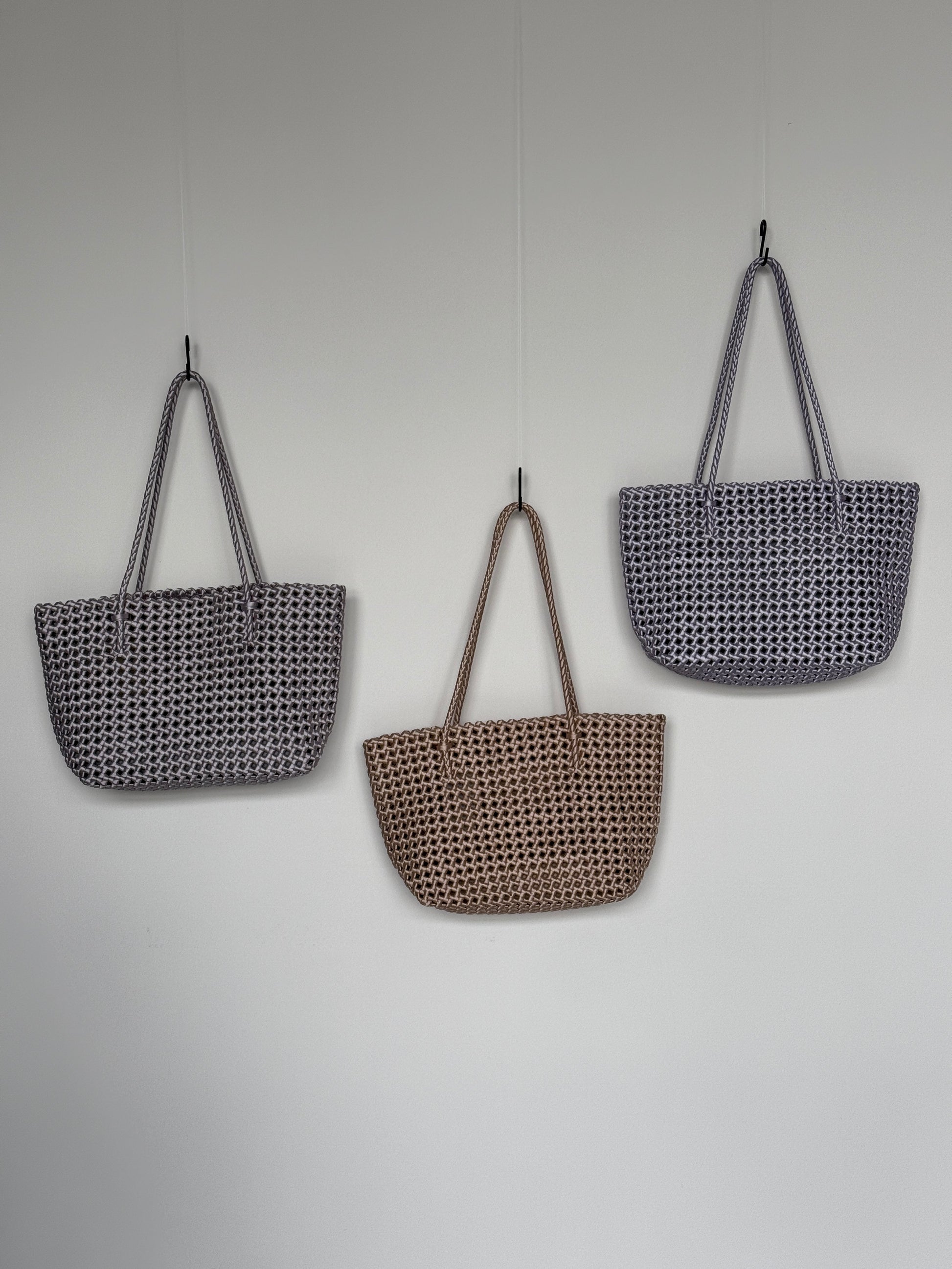 Drei Braided Shopper Bags in den Farben Silber, Gold und Flieder mit langem Henkel im geflochtenen Design an einer Wand hängend