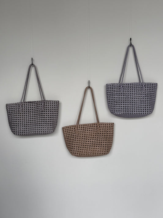 Drei Braided Shopper Bags in den Farben Silber, Gold und Flieder mit langem Henkel im geflochtenen Design an einer Wand hängend