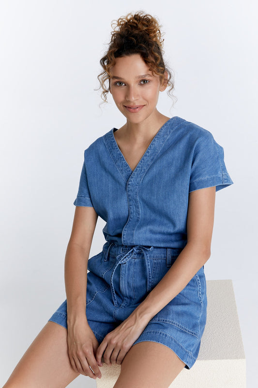 Damen Jumpsuit Shorts in Medium Blue von COJ – Vorderansicht im Sitzen mit V-Ausschnitt und Taillenzug