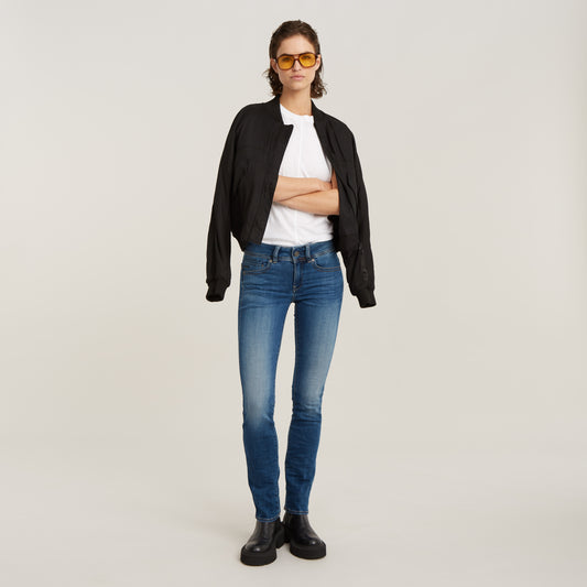 Komplettes Outfit mit der G-Star Midge Straight Jeans in Medium Indigo Aged, kombiniert mit einer schwarzen Jacke und gelben Brillen.
