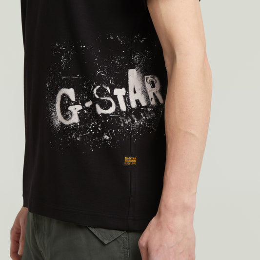 Detailansicht des G-Star Raw Sprayed T-Shirt - Black mit gesprühtem G-Star Logo-Print in Weiß und kleinem Label am Saum.