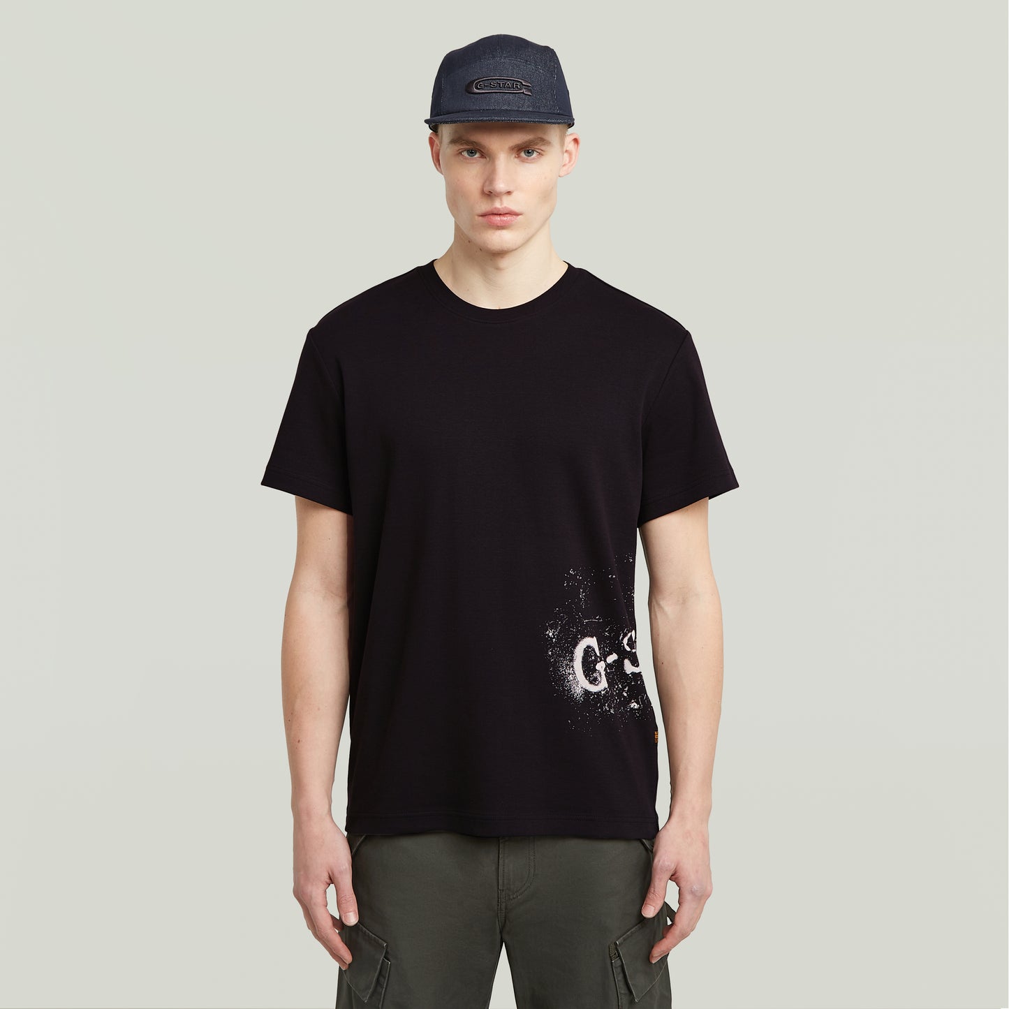 Vorderansicht des G-Star Raw Sprayed T-Shirt - Black, schwarzes T-Shirt mit weißem gesprühtem Logo-Print am unteren Saum.