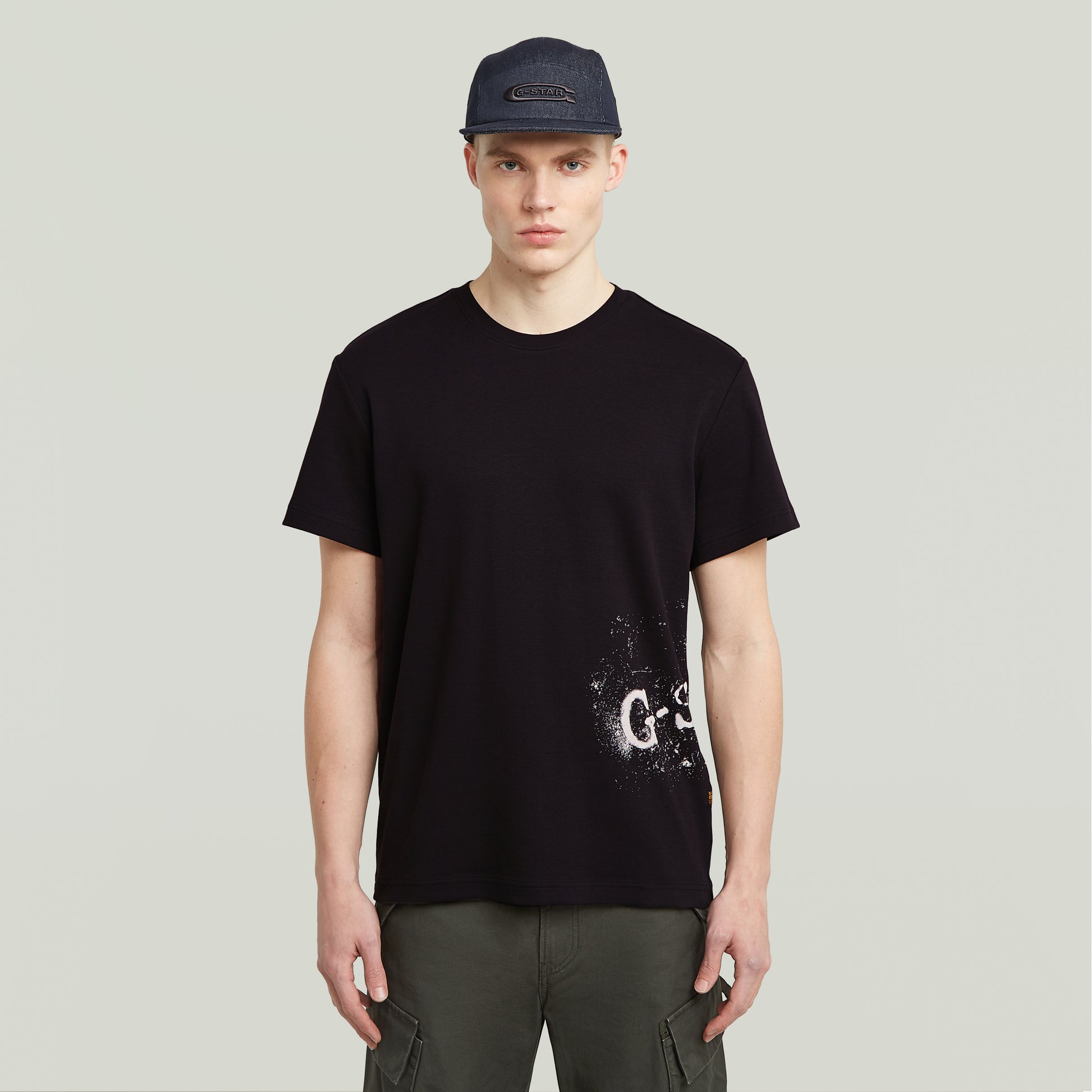 Vorderansicht des G-Star Raw Sprayed T-Shirt - Black, schwarzes T-Shirt mit weißem gesprühtem Logo-Print am unteren Saum.