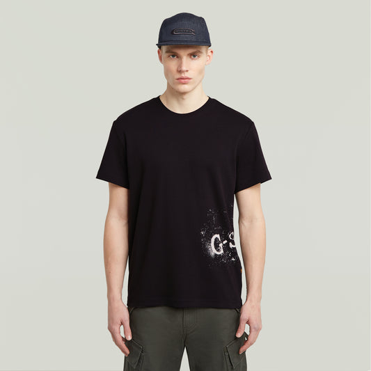 Vorderansicht des G-Star Raw Sprayed T-Shirt - Black, schwarzes T-Shirt mit weißem gesprühtem Logo-Print am unteren Saum.