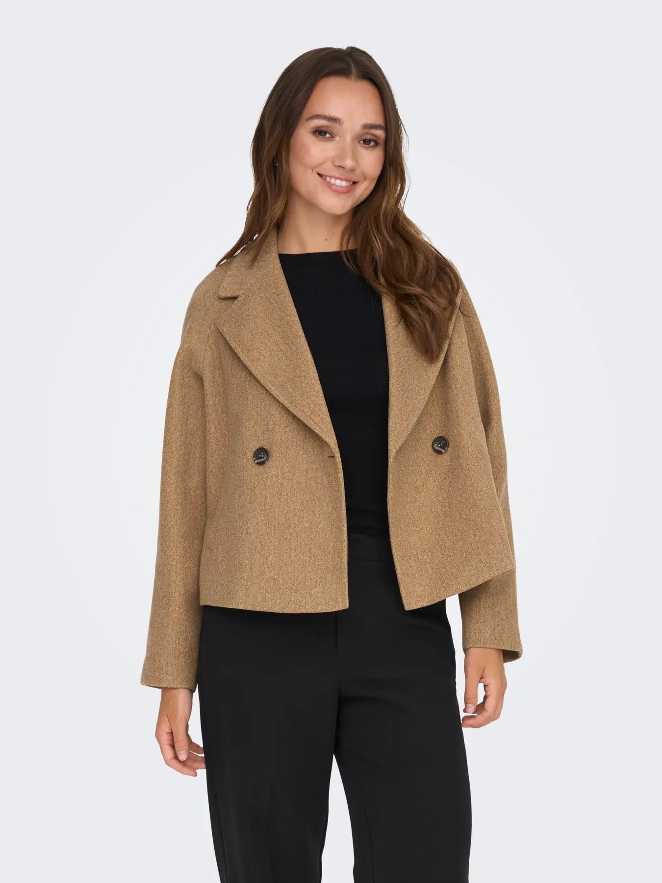 Frau kombiniert die JDY Viola Life Short Jacket Camel Melange mit schwarzer Hose für einen eleganten Look.