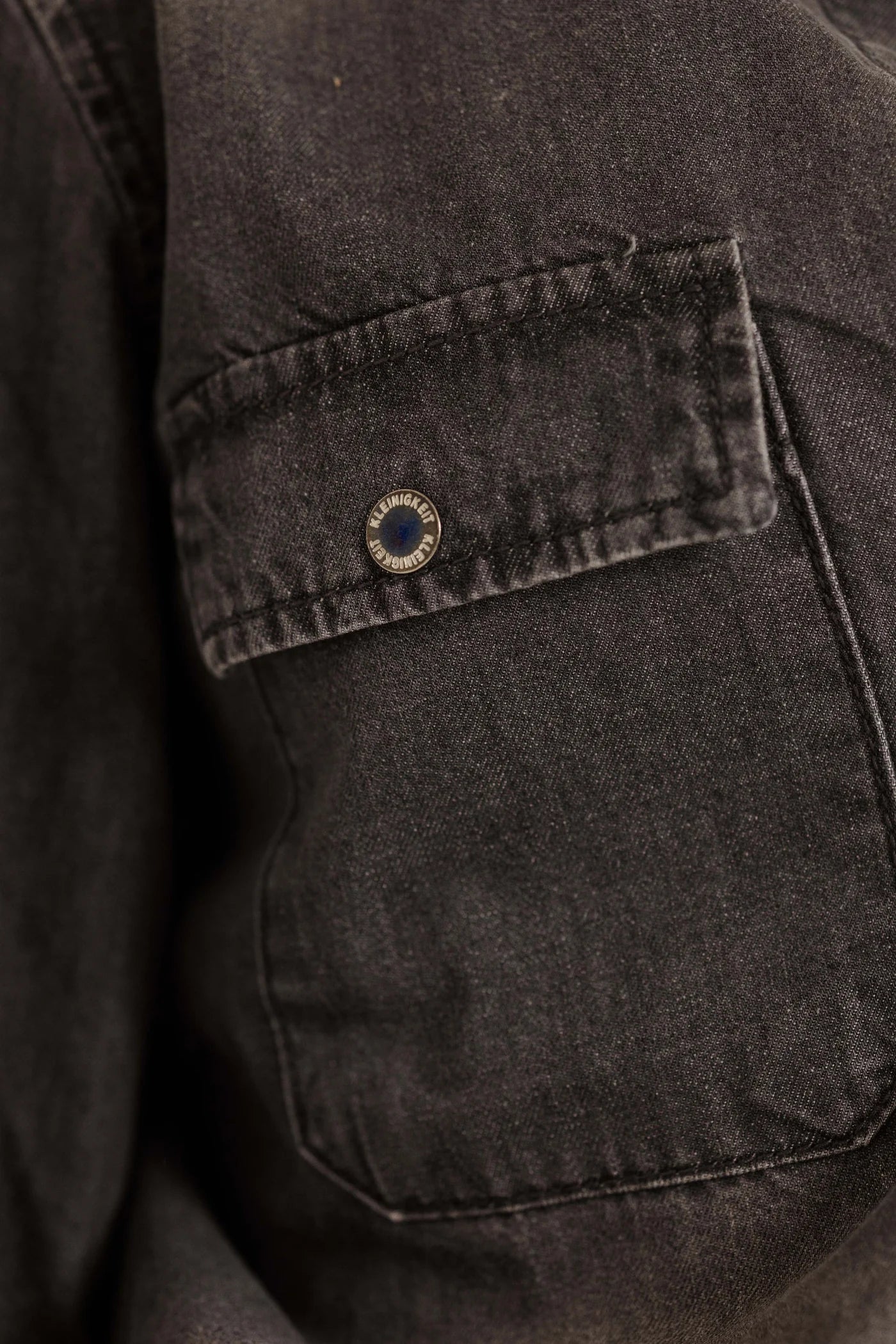 Nahaufnahme des Kleinigkeit Denim Moore Overshirts, mit Fokus auf eine Brusttasche und den markanten Knopf mit Kleinigkeit-Logo.