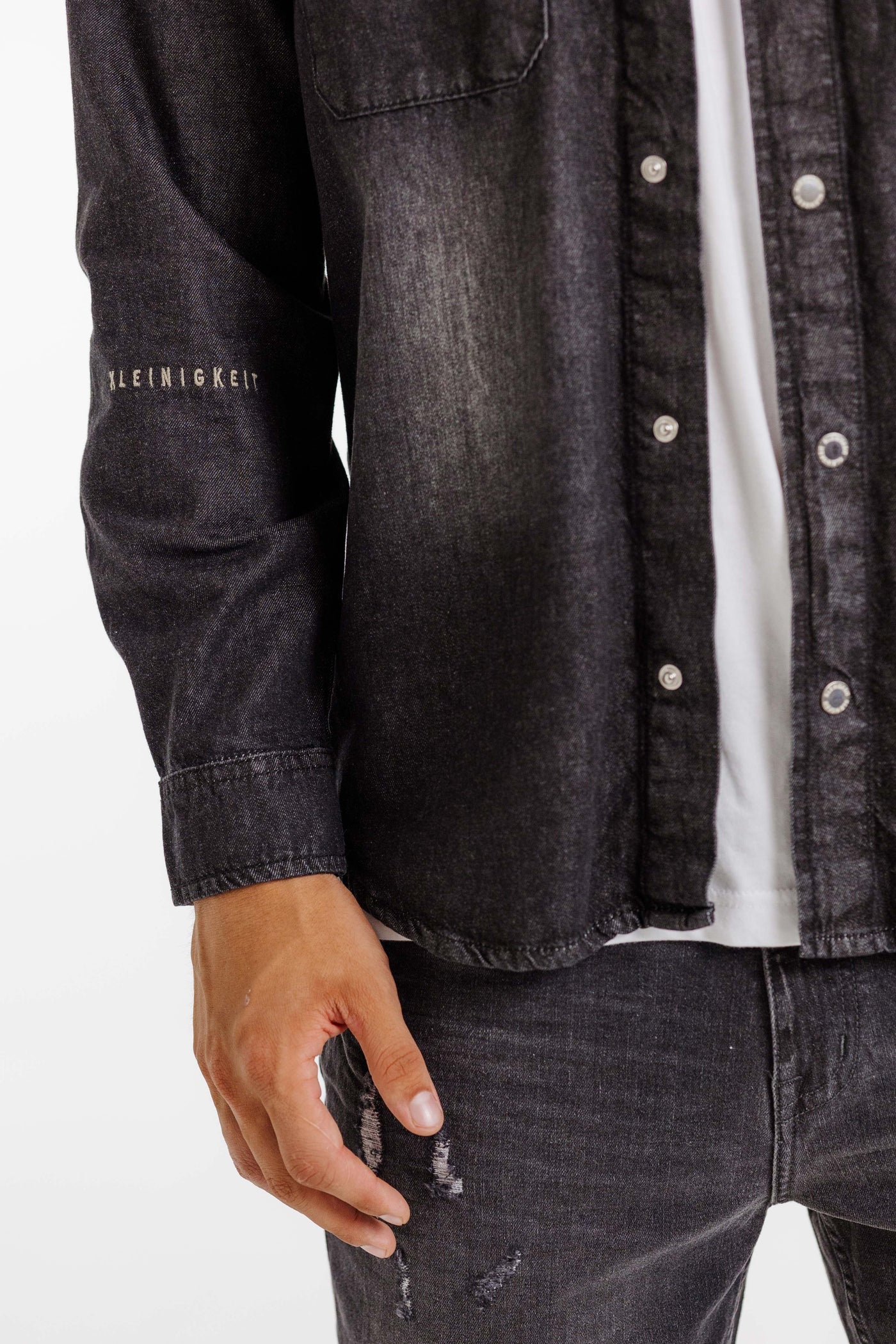 Nahaufnahme des Ärmels des Kleinigkeit Jürgen Jeansmann Overshirts in Grau mit gesticktem Kleinigkeit-Logo.