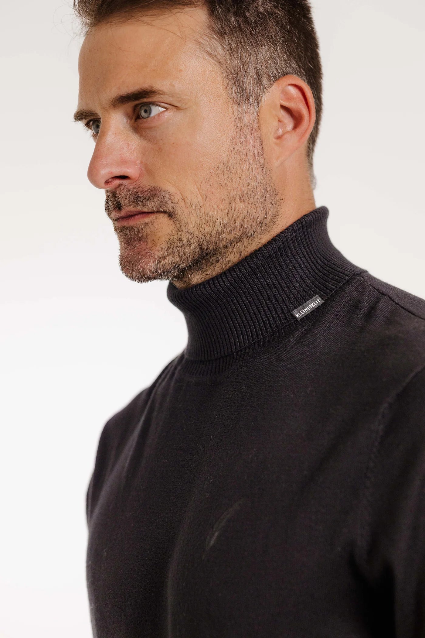 Nahaufnahme des Kleinigkeit Rolliver Kahn Rollkragenpullovers in Schwarz mit Flaglabel und feiner Stickerei.