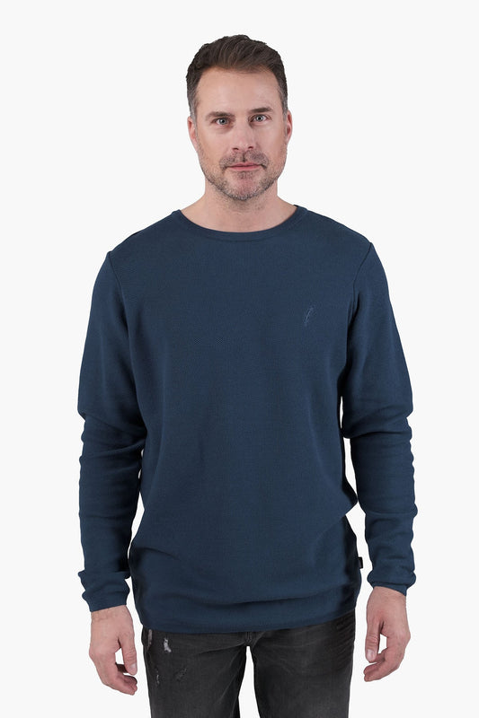 Modell trägt den Kleinigkeit Stricktease Dark Blue Pullover – luftiger, dunkelblauer Strickpullover mit gestickter Feder auf der Brust aus grober Baumwollqualität.