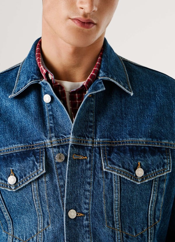 Detailaufnahme der Pepe Jeans London Regular Jacket - Denim: blaue Denimjacke mit markanten Kontrastnähten, Metallknöpfen und aufgesetzten Brusttaschen.