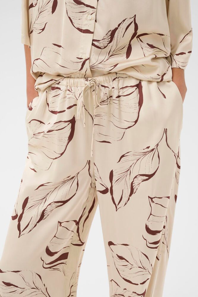Detailaufnahme der Soaked Clero Flared Printed Pants - Oatmeal Leave Print mit elastischem Bund, Bindeband und floralem Muster